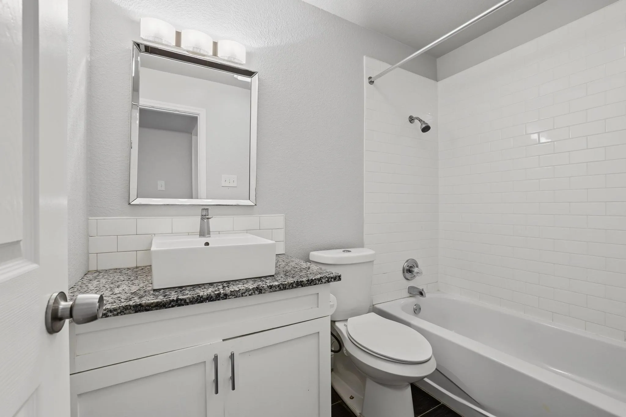 Bathroom featuring a white subway tile shower surround, a white vanity with a granite countertop, a vessel sink, and a framed mirror with contemporary lighting