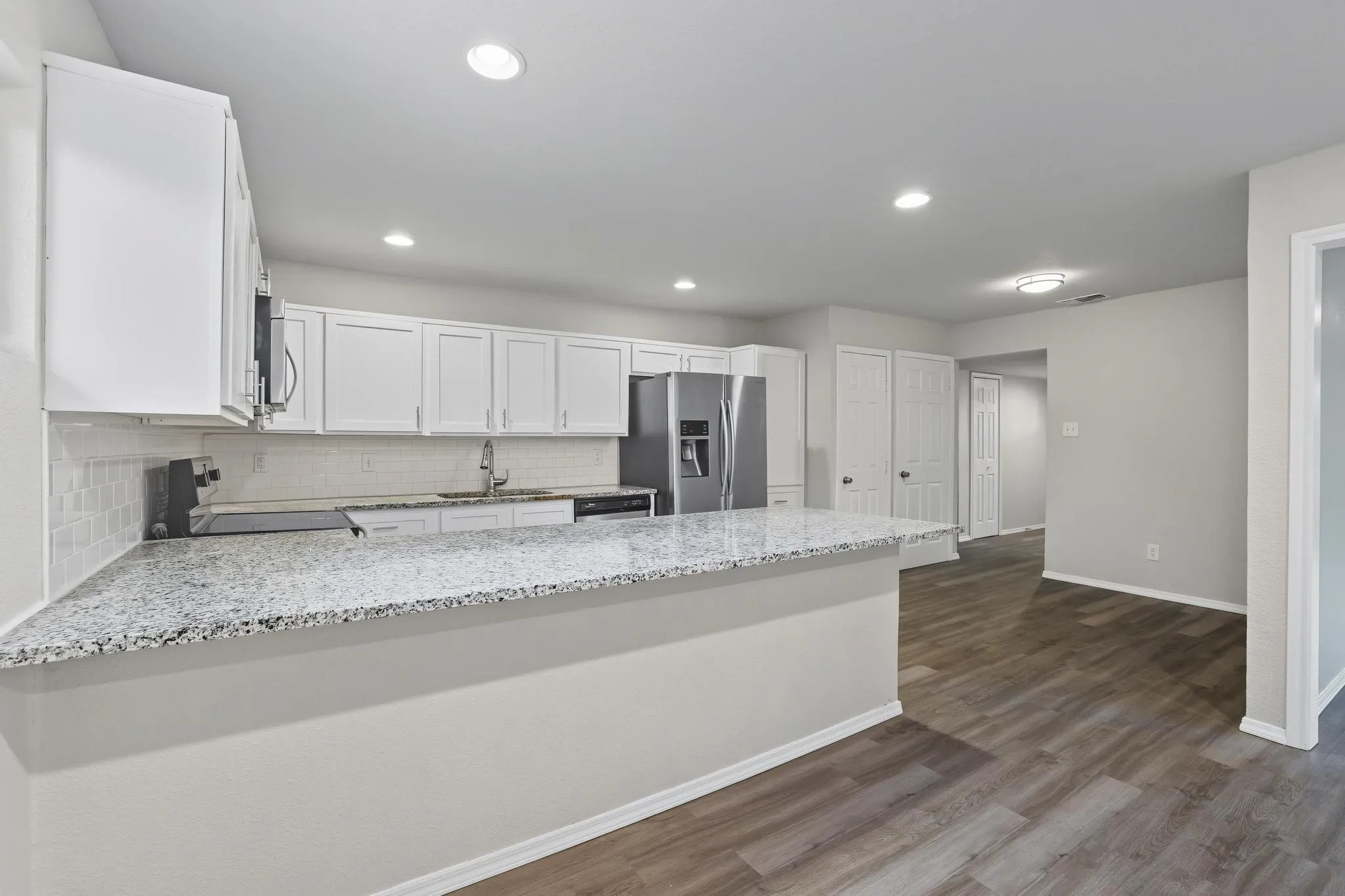 Kitchen featuring white shaker cabinetry, speckled countertops, a subway tile backsplash, stainless steel appliances, and wood-finish flooring
