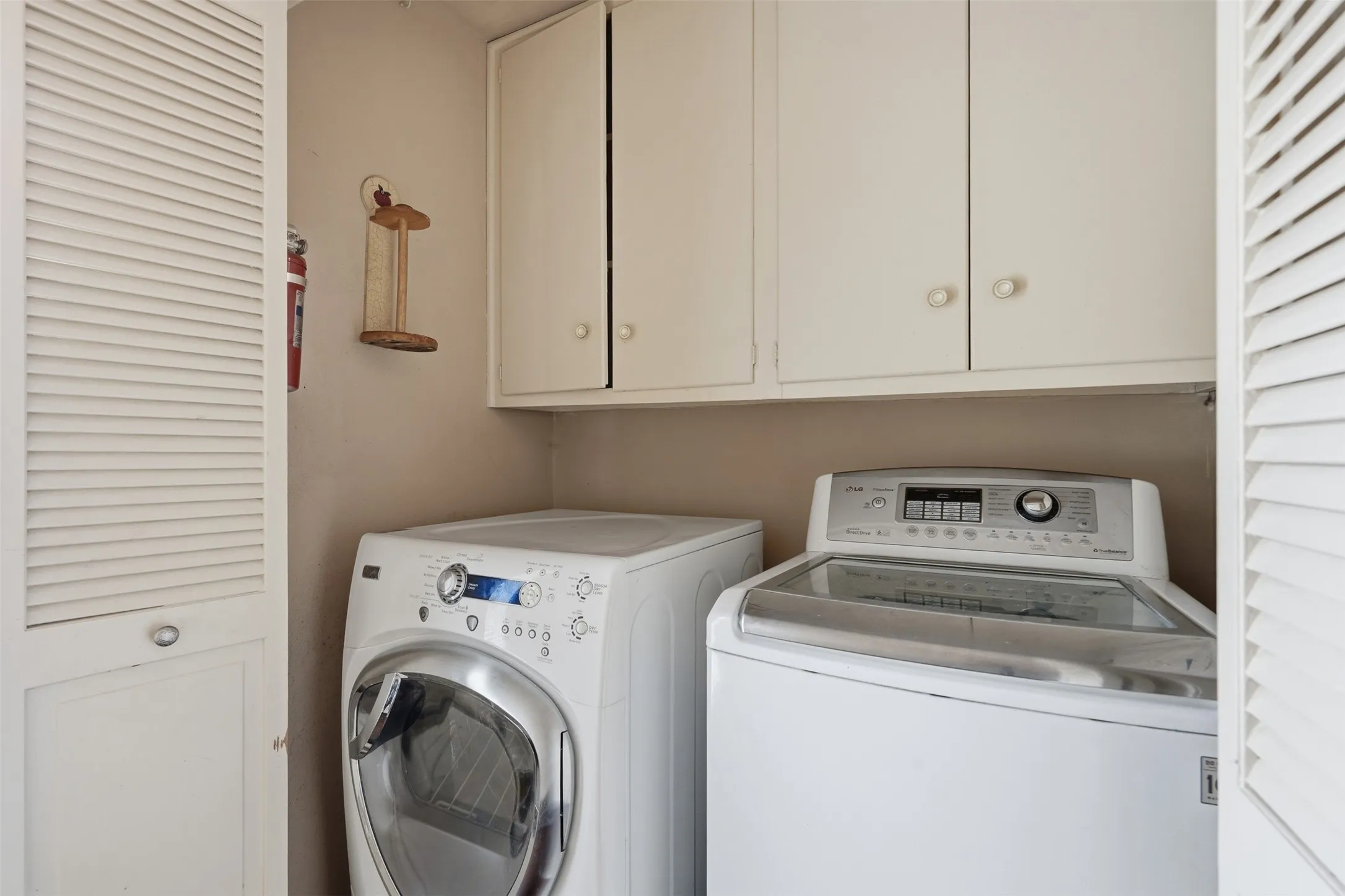 Dedicated laundry area featuring a front-load washing machine, top-load washing machine, and upper cabinetry