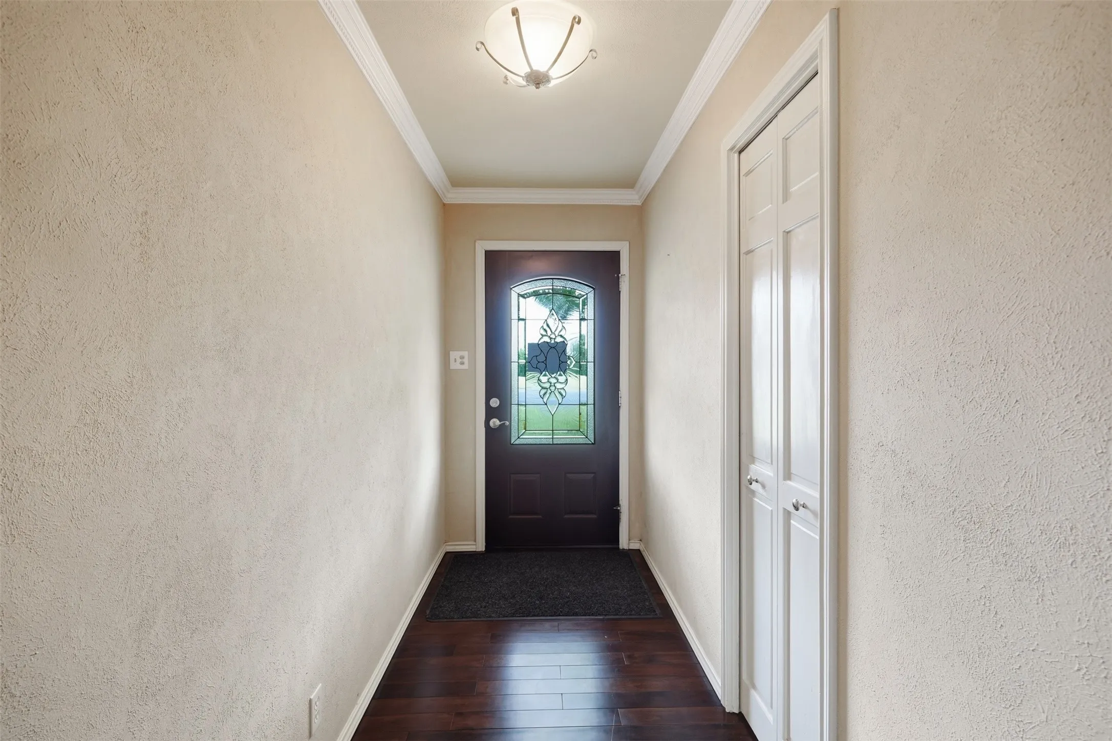 Entryway featuring dark wood-finish flooring, textured walls, and crown molding