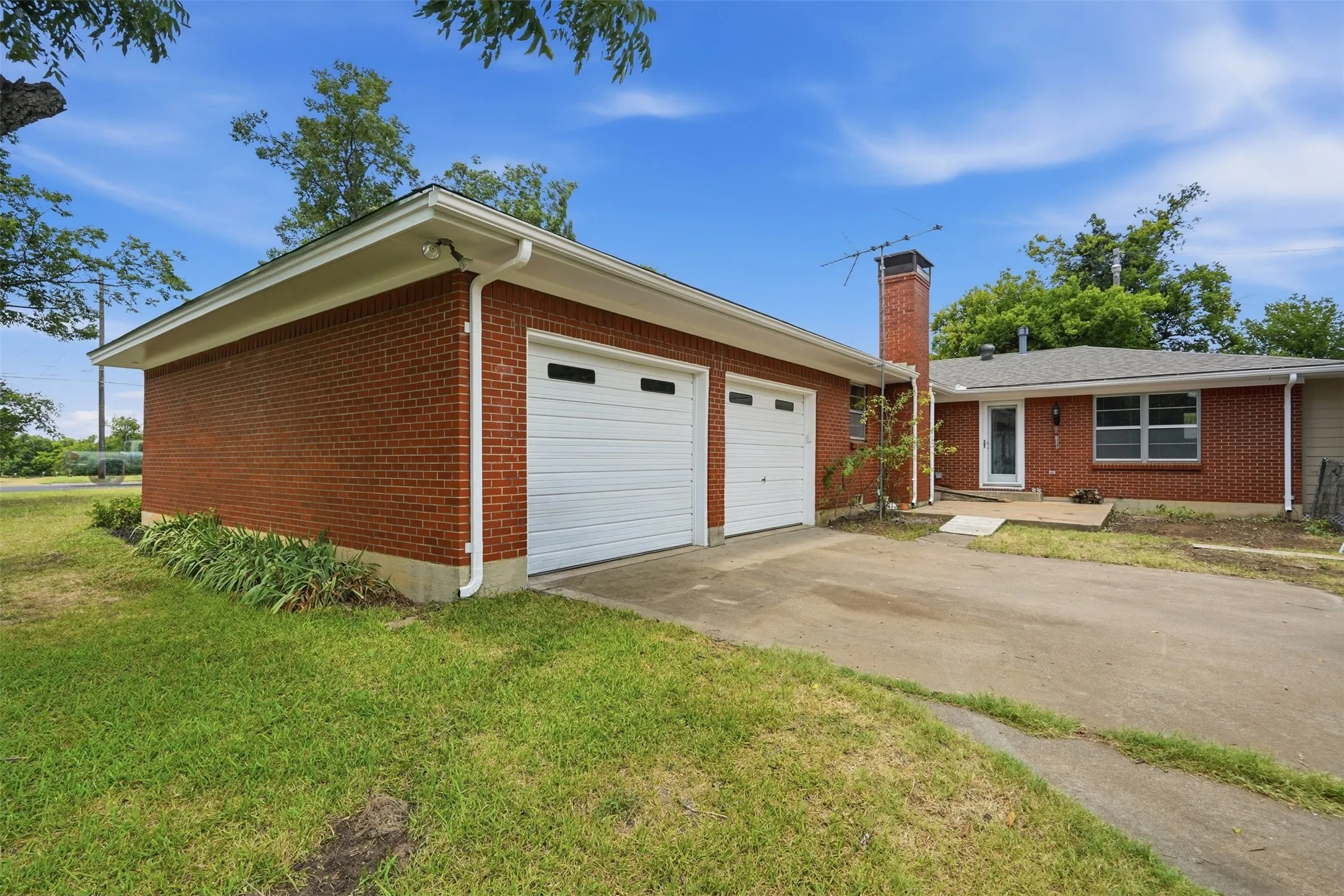 Brick exterior featuring a two-car garage with white doors, a concrete driveway, and a red brick chimney