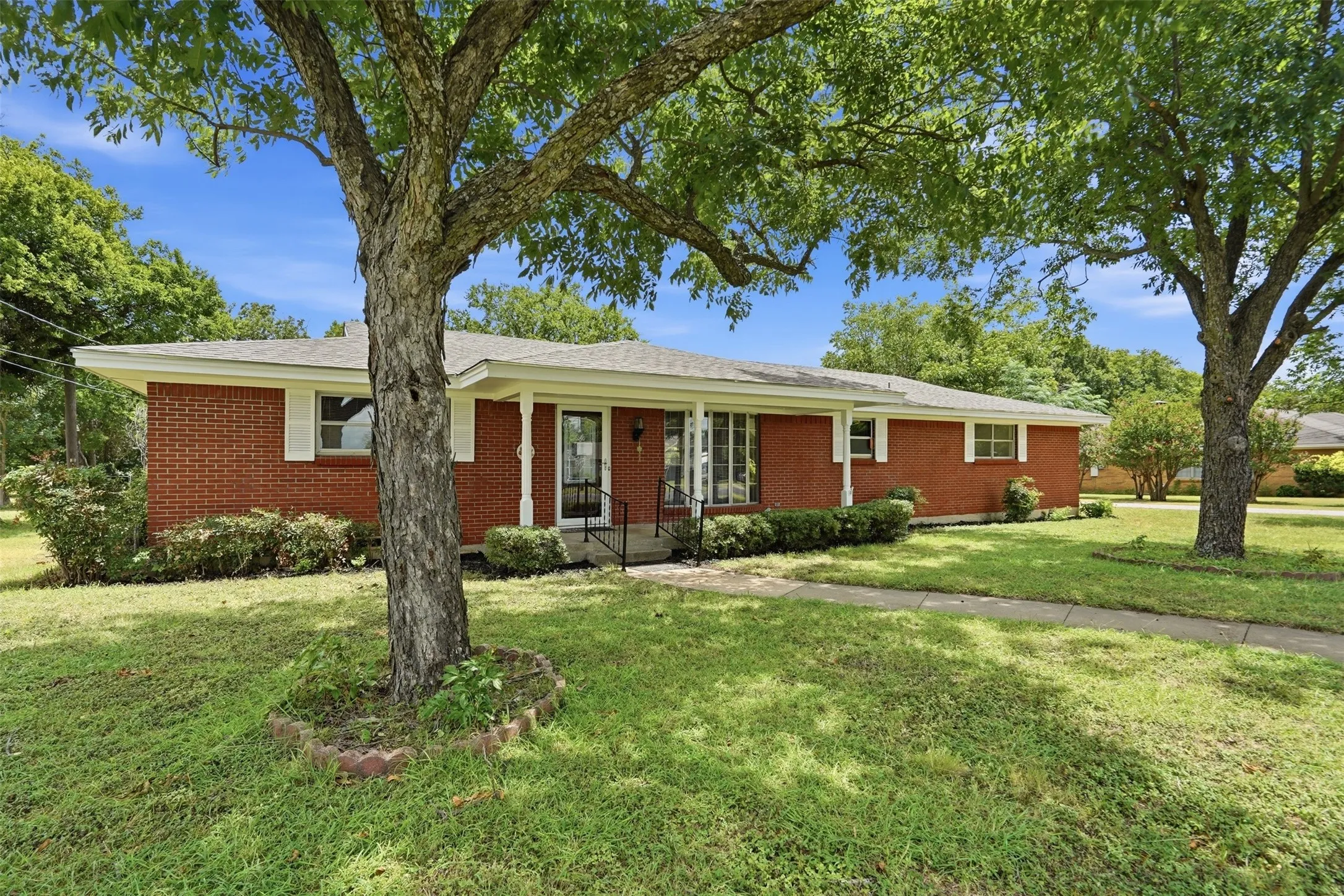 Red brick exterior featuring white window shutters, a covered entry porch, and a sidewalk leading to the front door