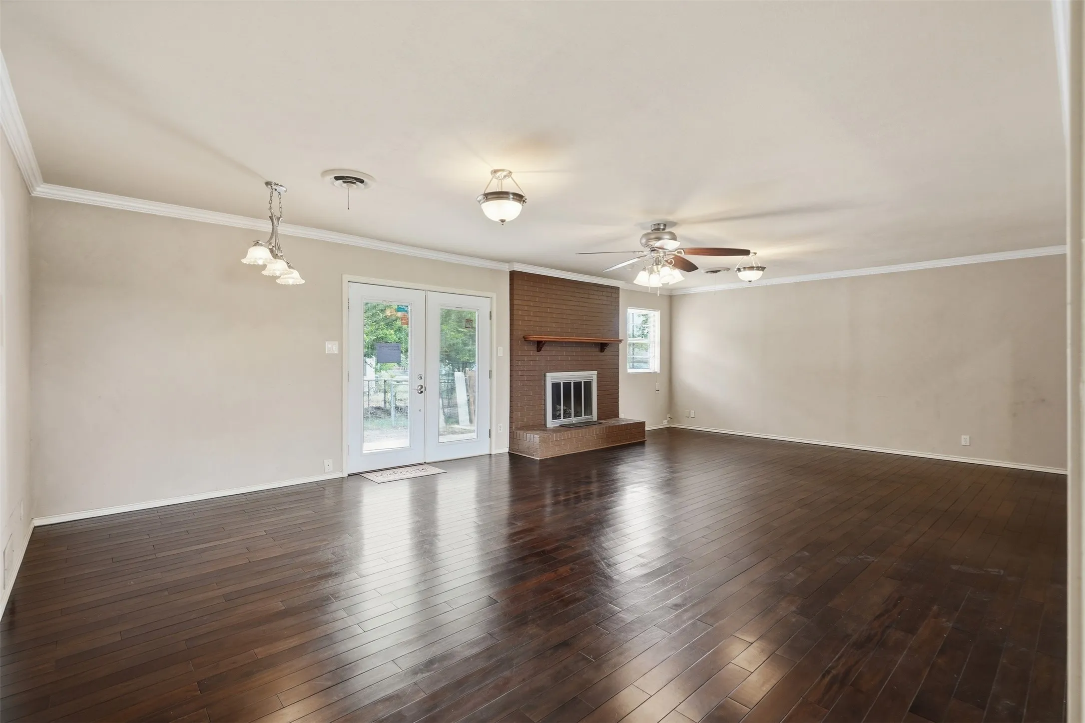 Spacious room featuring dark wood-finish flooring, a brick fireplace with a wood mantel, and white French doors
