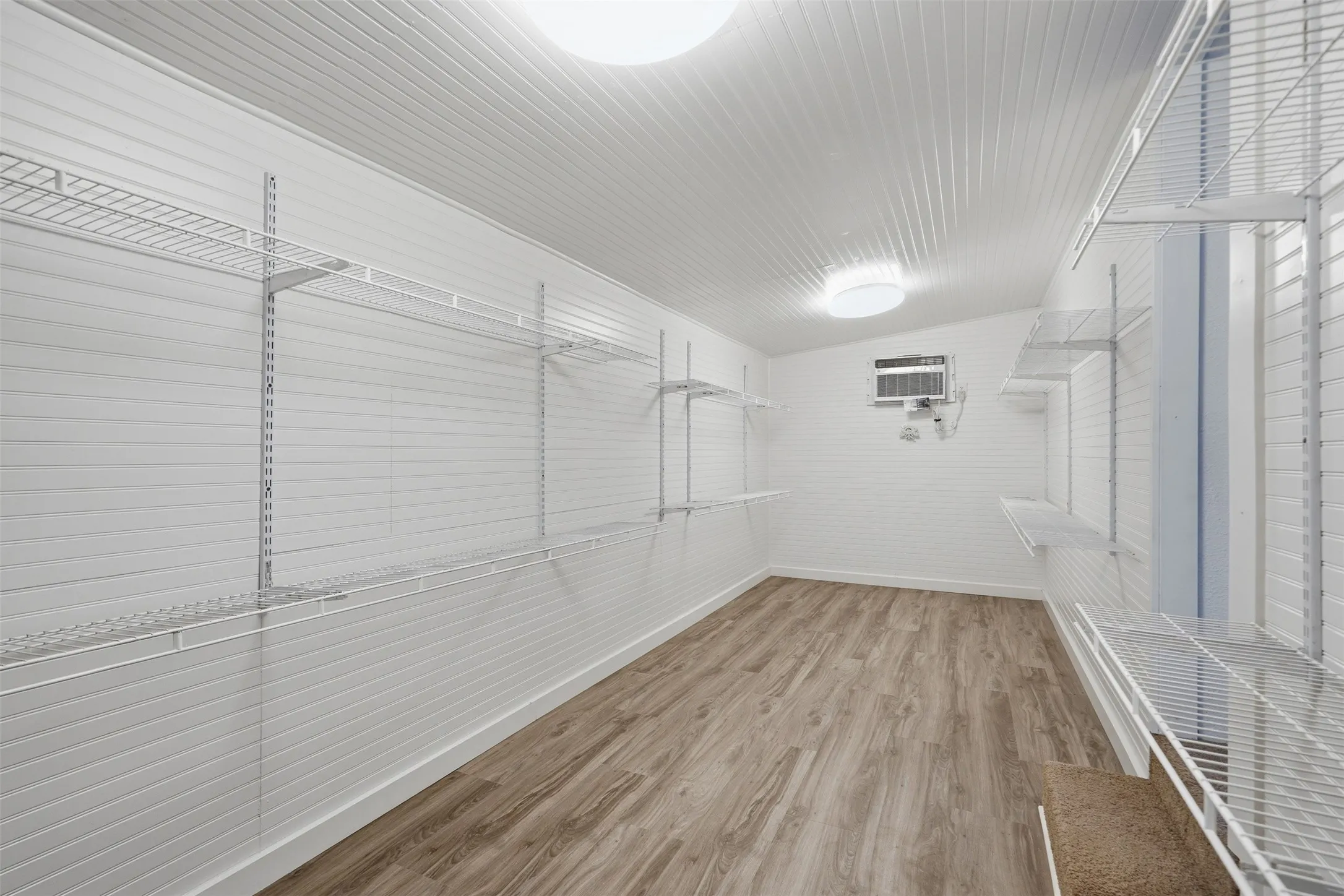 Expansive storage room featuring wood-finish flooring, white panel walls, and multiple levels of wire shelving for customizable organization