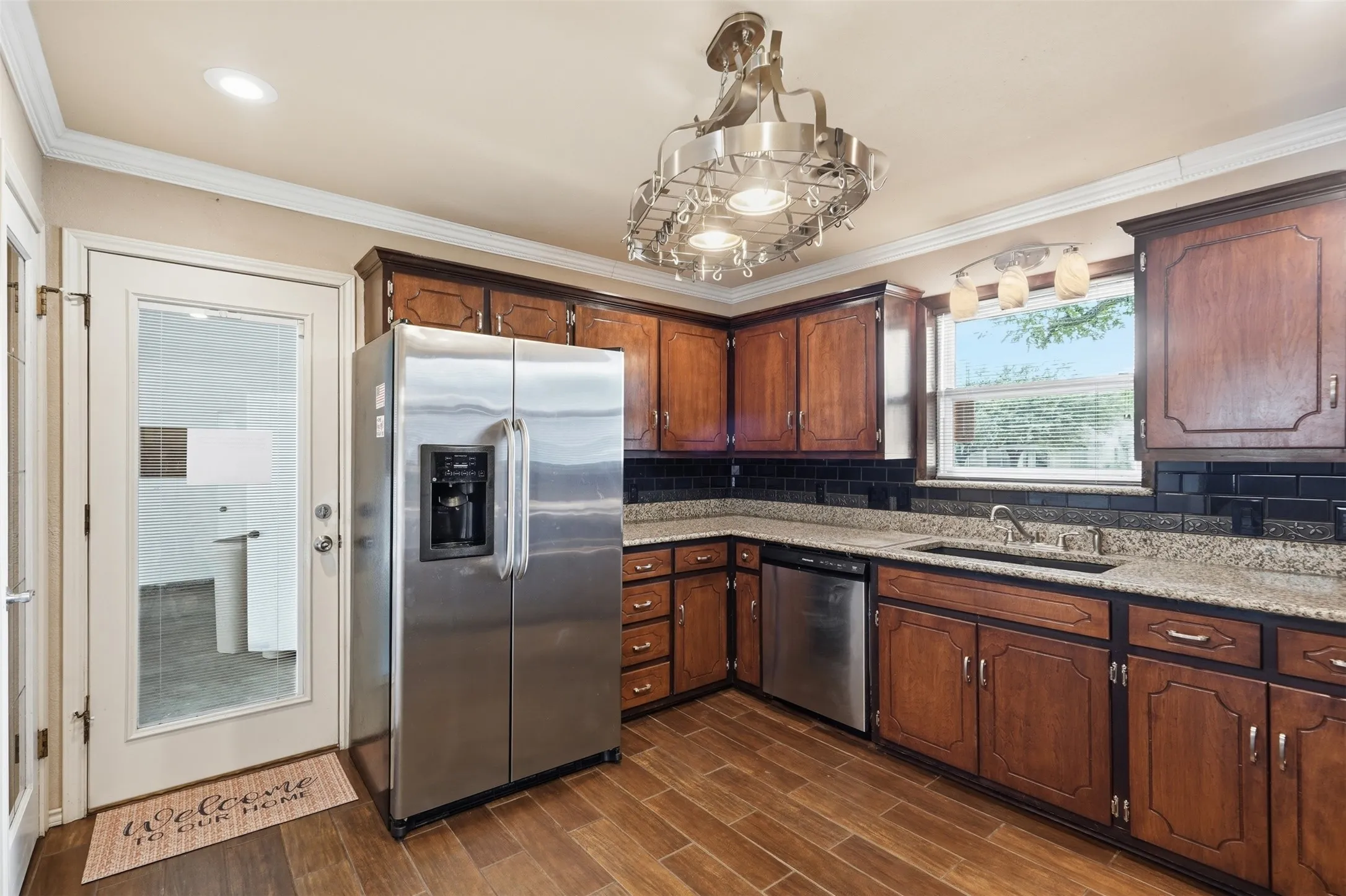 Kitchen featuring wood-finish flooring, granite-style countertops, dark wood cabinetry, a black subway tile backsplash, and stainless steel appliances