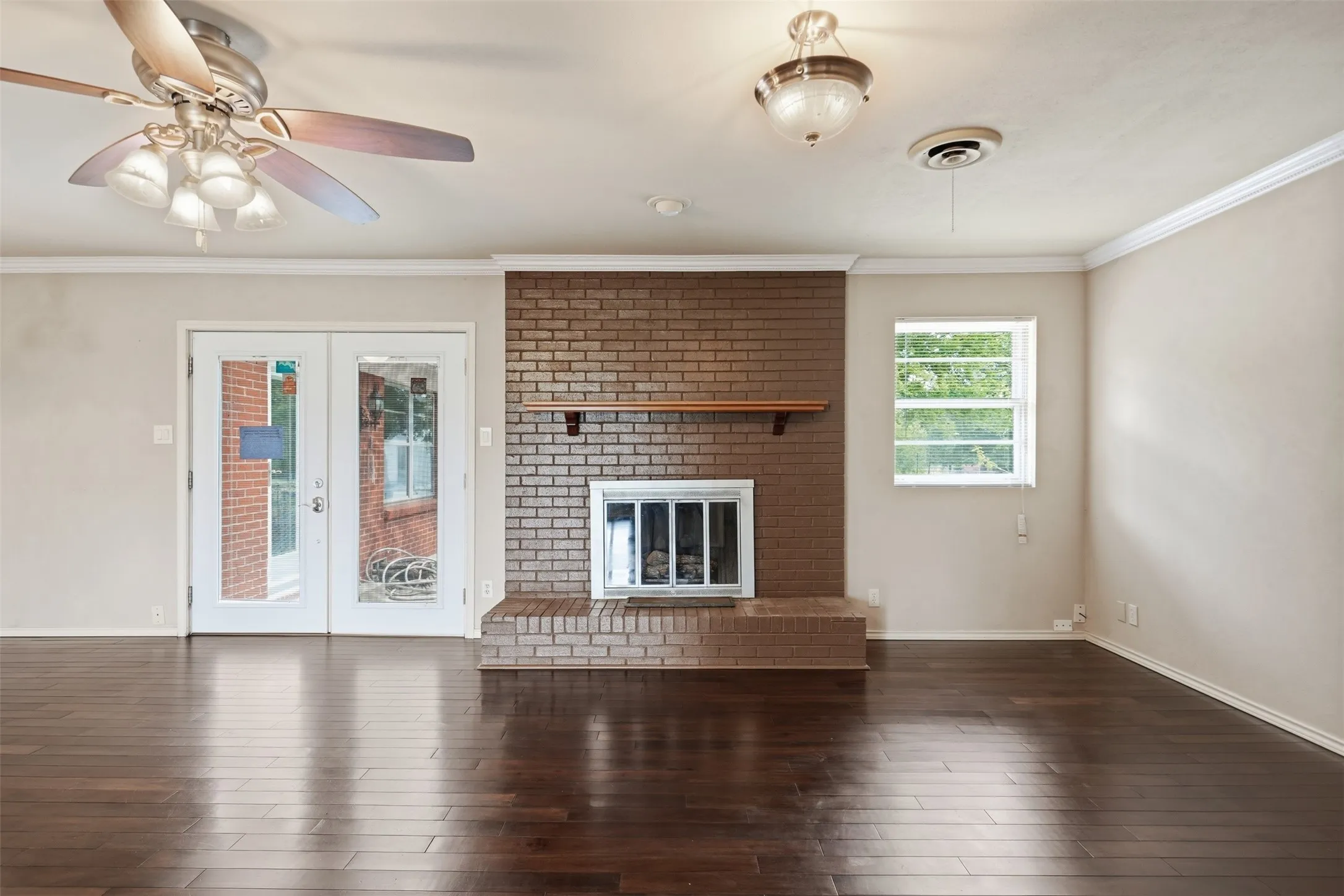 Spacious room featuring dark wood-finish flooring, a brick fireplace with a wood mantle, and glass-paneled French doors