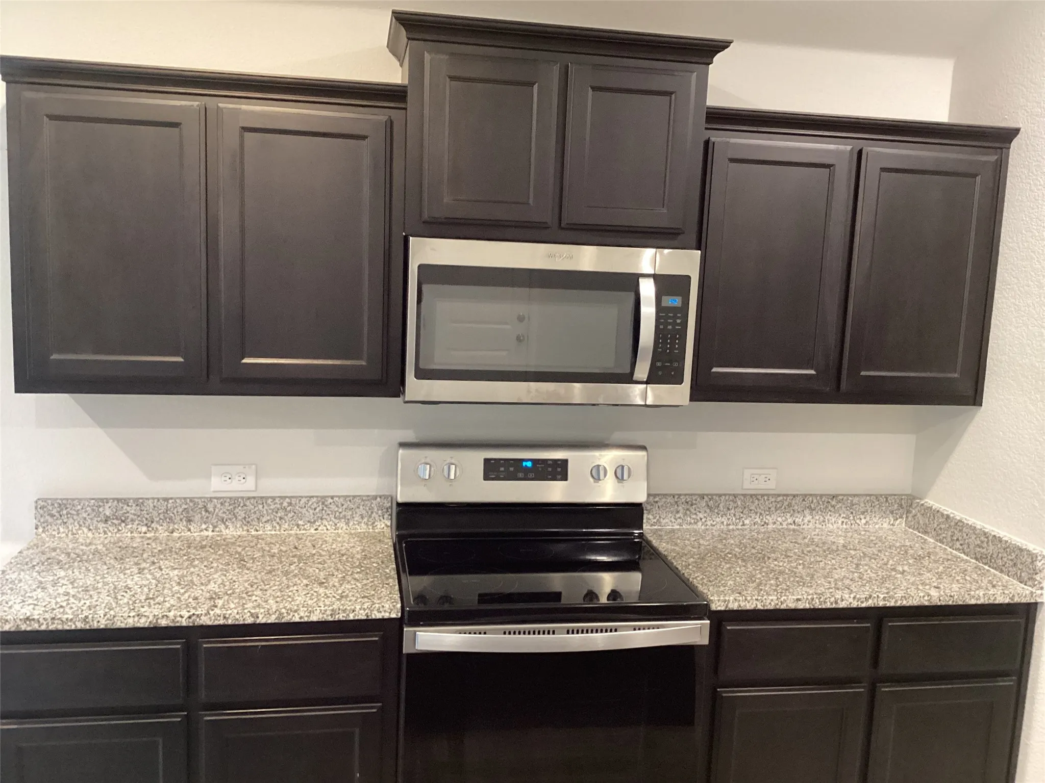 Kitchen featuring dark cabinetry, speckled countertops, stainless steel microwave, and electric range