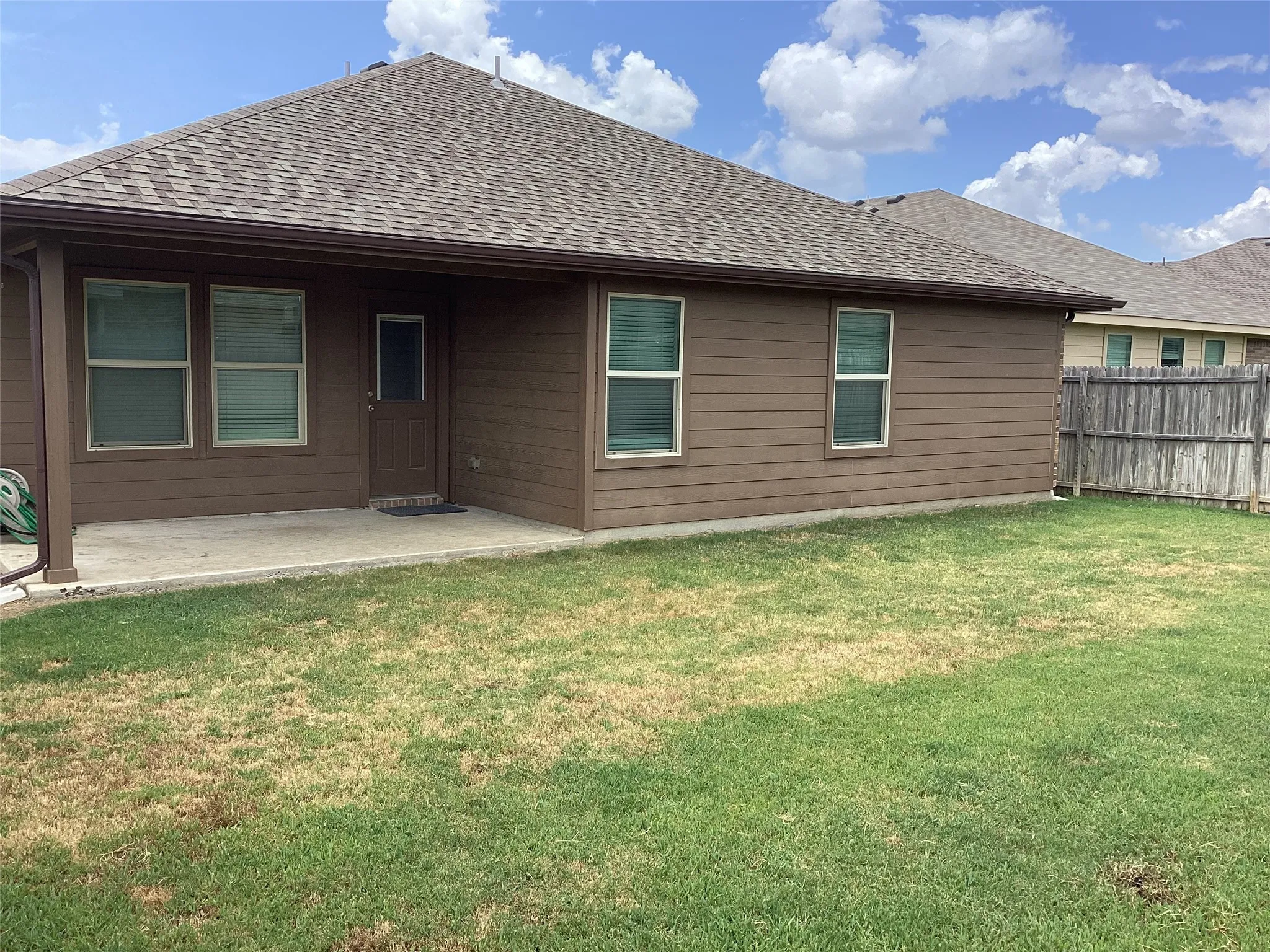 Spacious backyard with a concrete patio, brown siding, a covered porch area, and a privacy fence