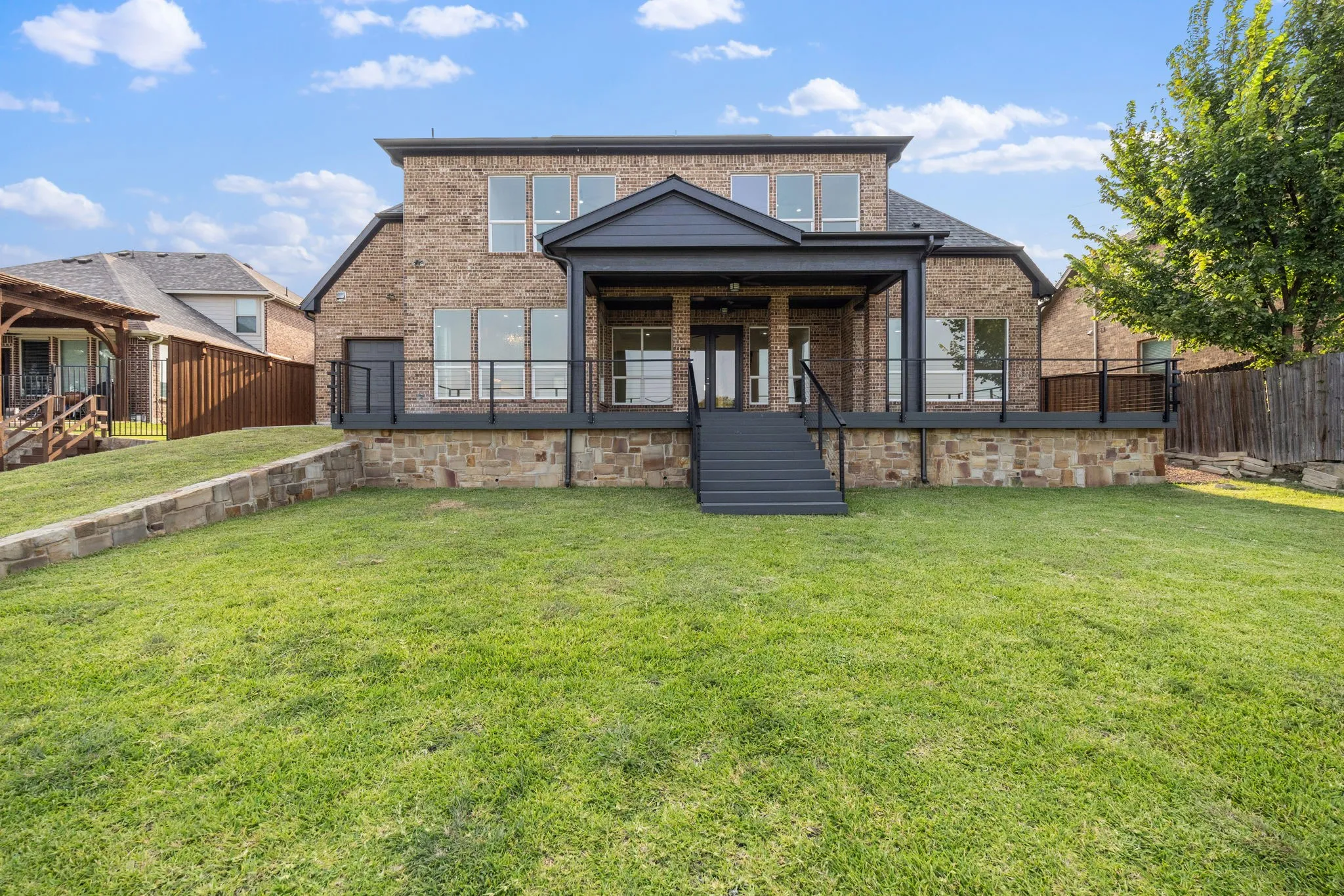 Impressive brick and stone exterior with a modern covered porch featuring black metal railings and substantial stone foundation