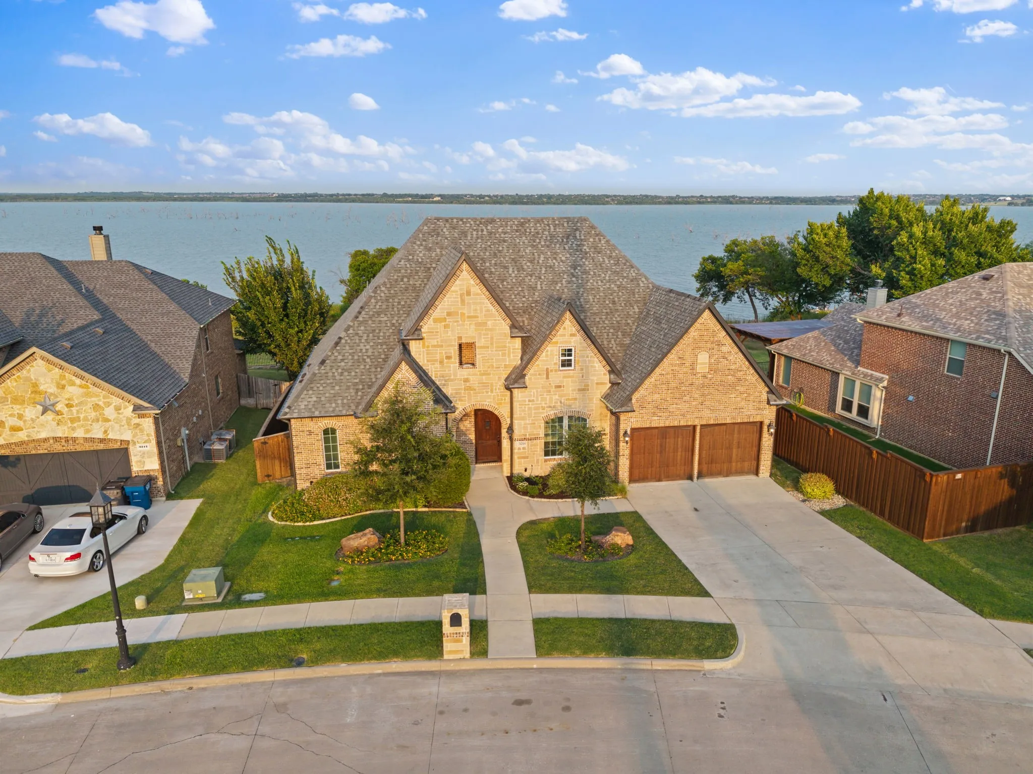 Elegant two-story brick residence featuring a steeply pitched roof with composite shingles, arched entryway with stone detailing, and a three-car attached garage