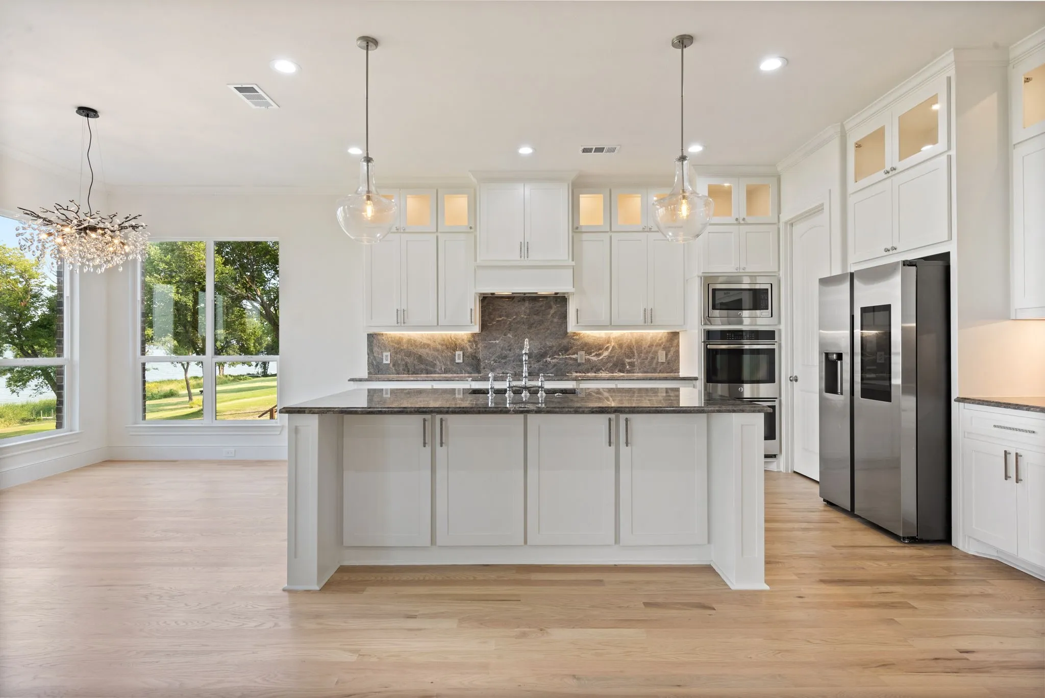 Spacious kitchen featuring an expansive center island with a dark countertop, white cabinetry with integrated lighting, stainless steel appliances, and a dark stone backsplash