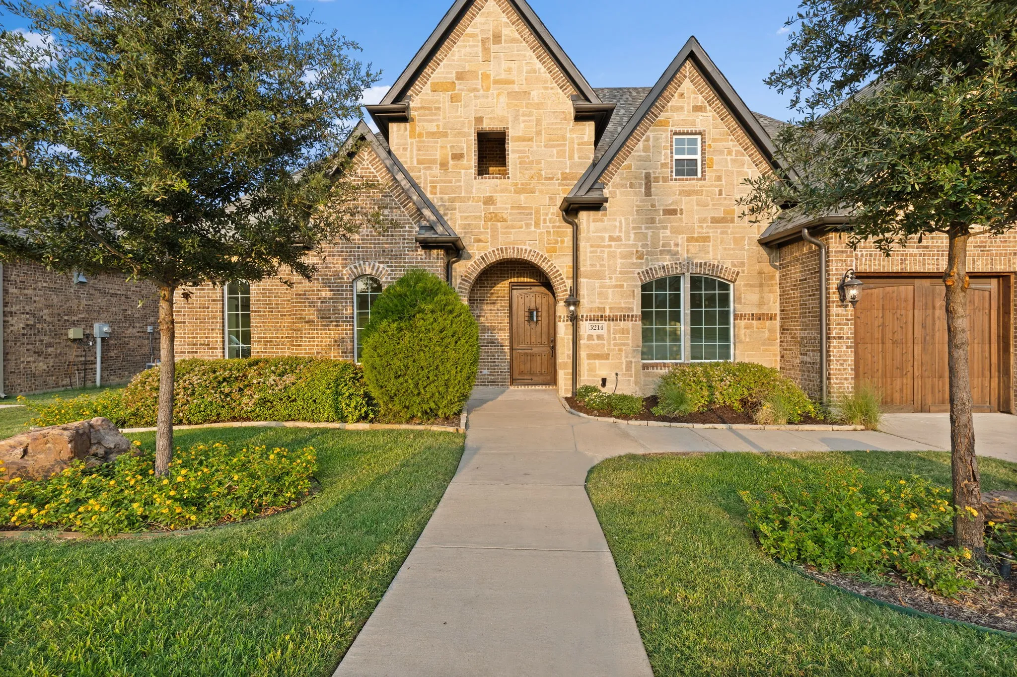 Stone and brick facade with gabled roofline, arched entry, decorative wood door, and arched window accents