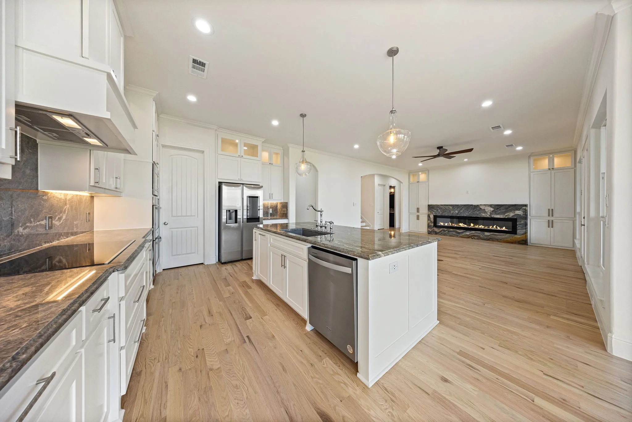 Open-concept interior featuring a spacious kitchen island with a dark stone countertop, integrated stainless steel appliances, and light wood-finish flooring