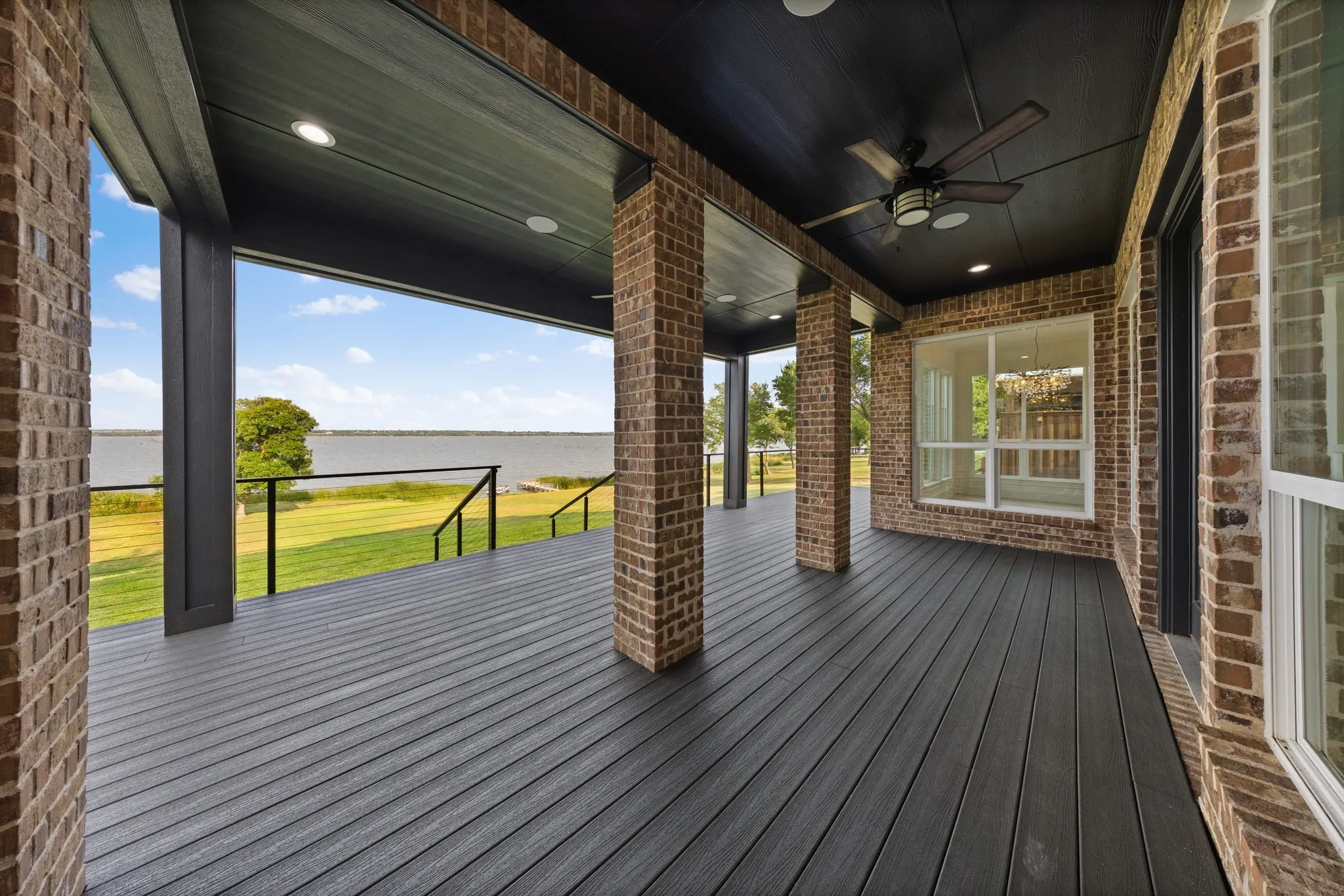 Covered outdoor deck with brick pillars, dark composite decking, a ceiling fan, recessed lighting, and expansive water frontage