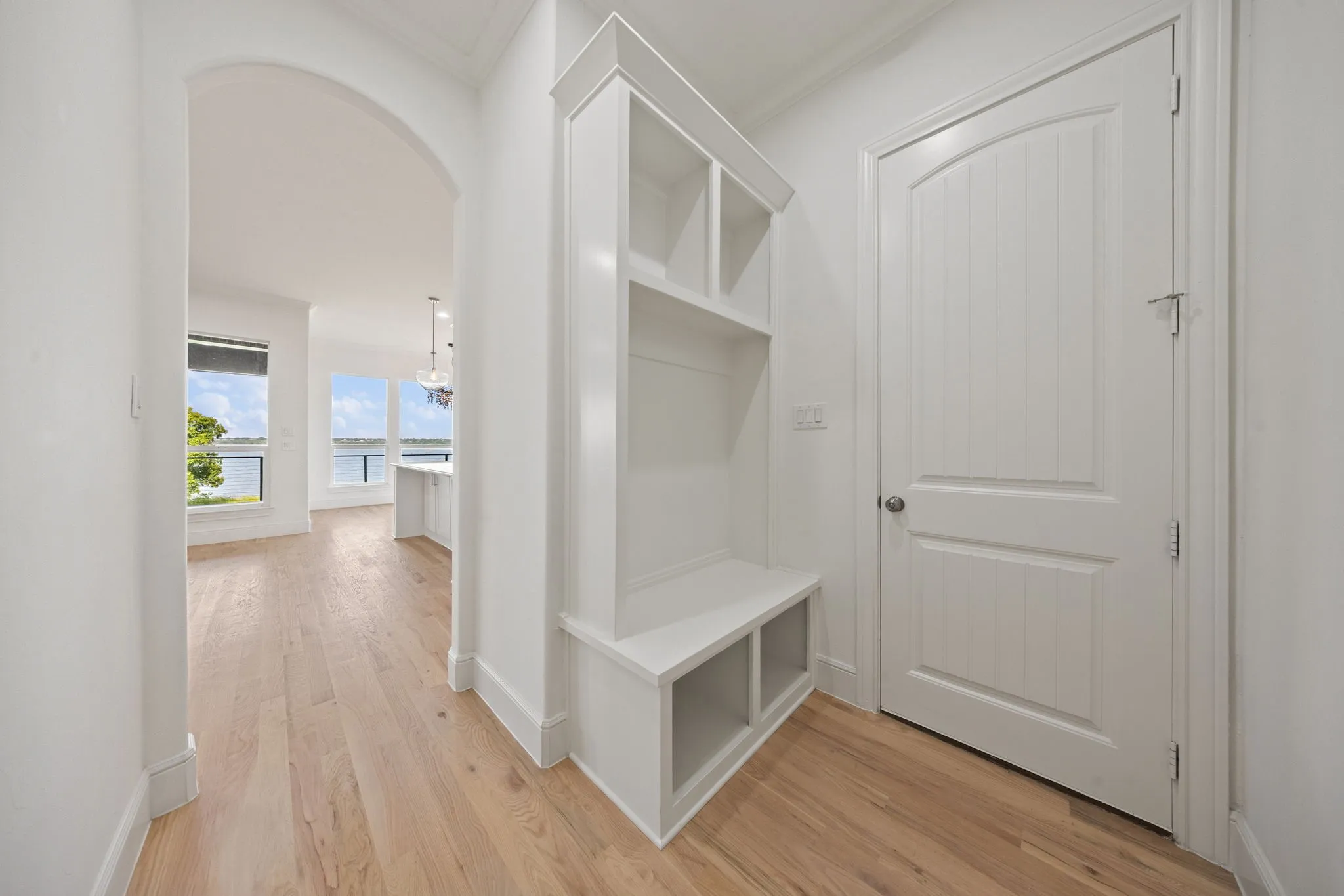 Entryway featuring a built-in white storage bench with open shelving, wood-finish flooring, and crisp white trim