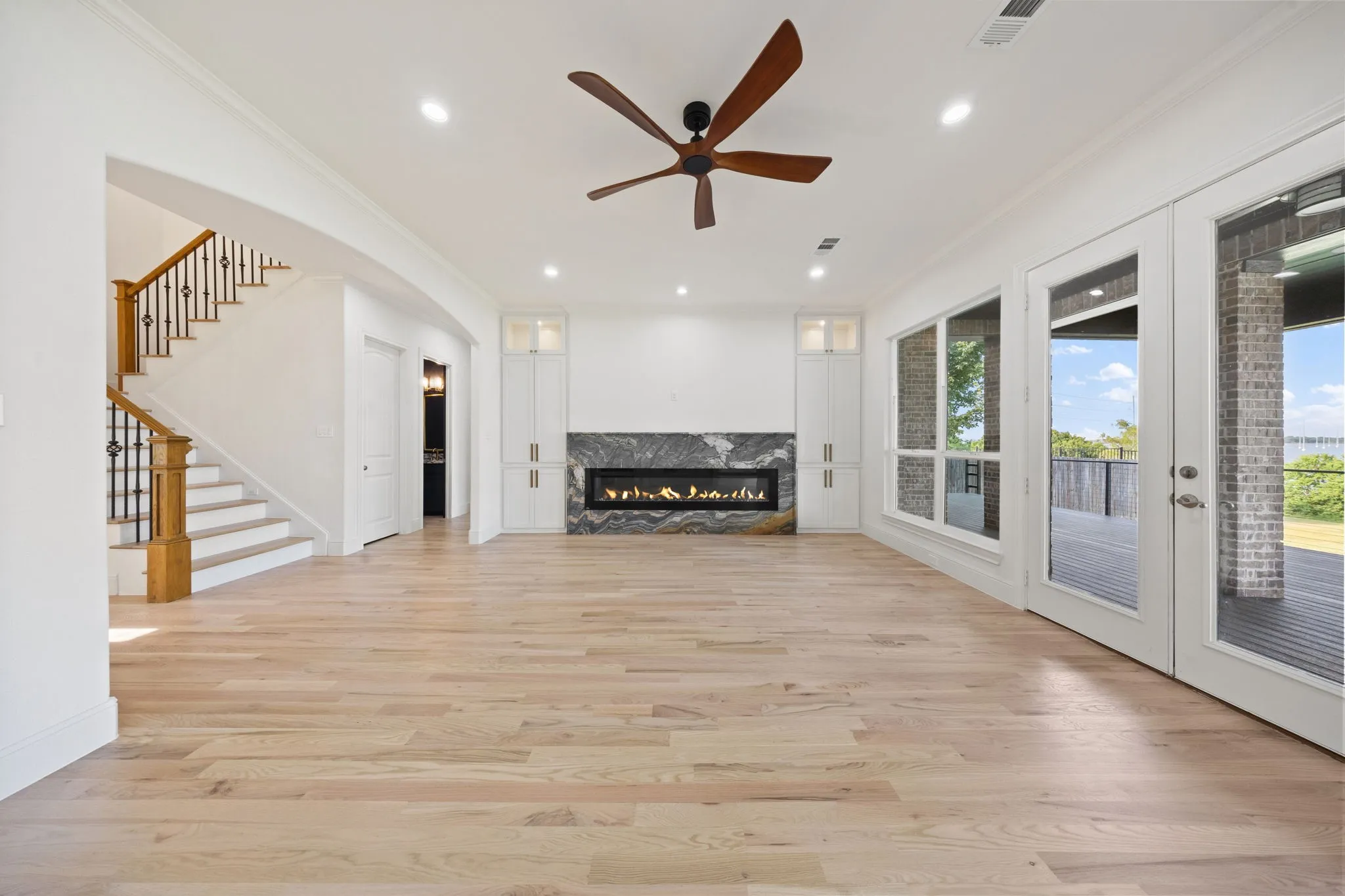 Spacious interior with light wood-finish flooring, a linear fireplace with a dark stone surround, and built-in white cabinetry