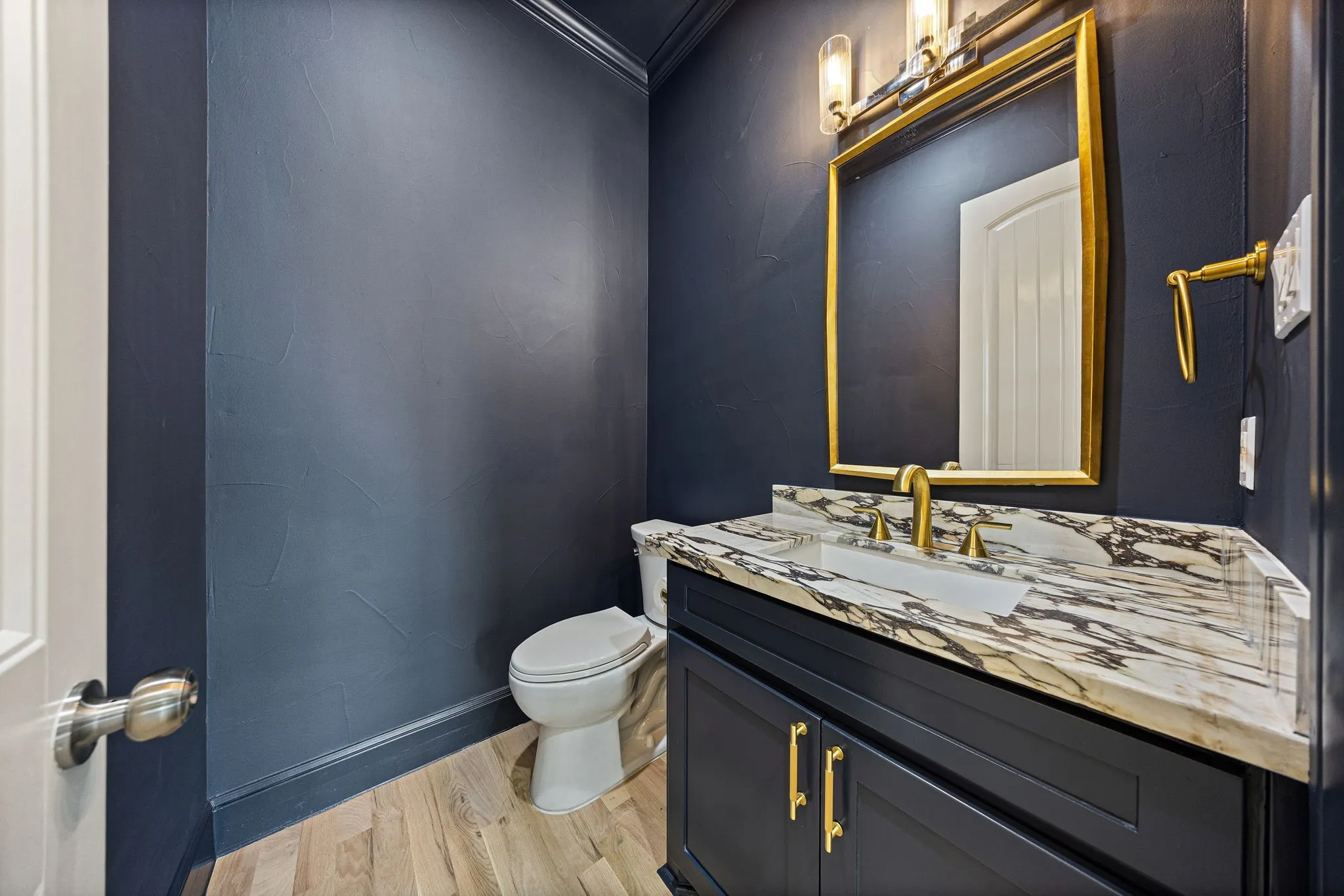 Bathroom featuring a vanity with a white and gray veined countertop, gold-toned faucet, and a large gold-framed mirror