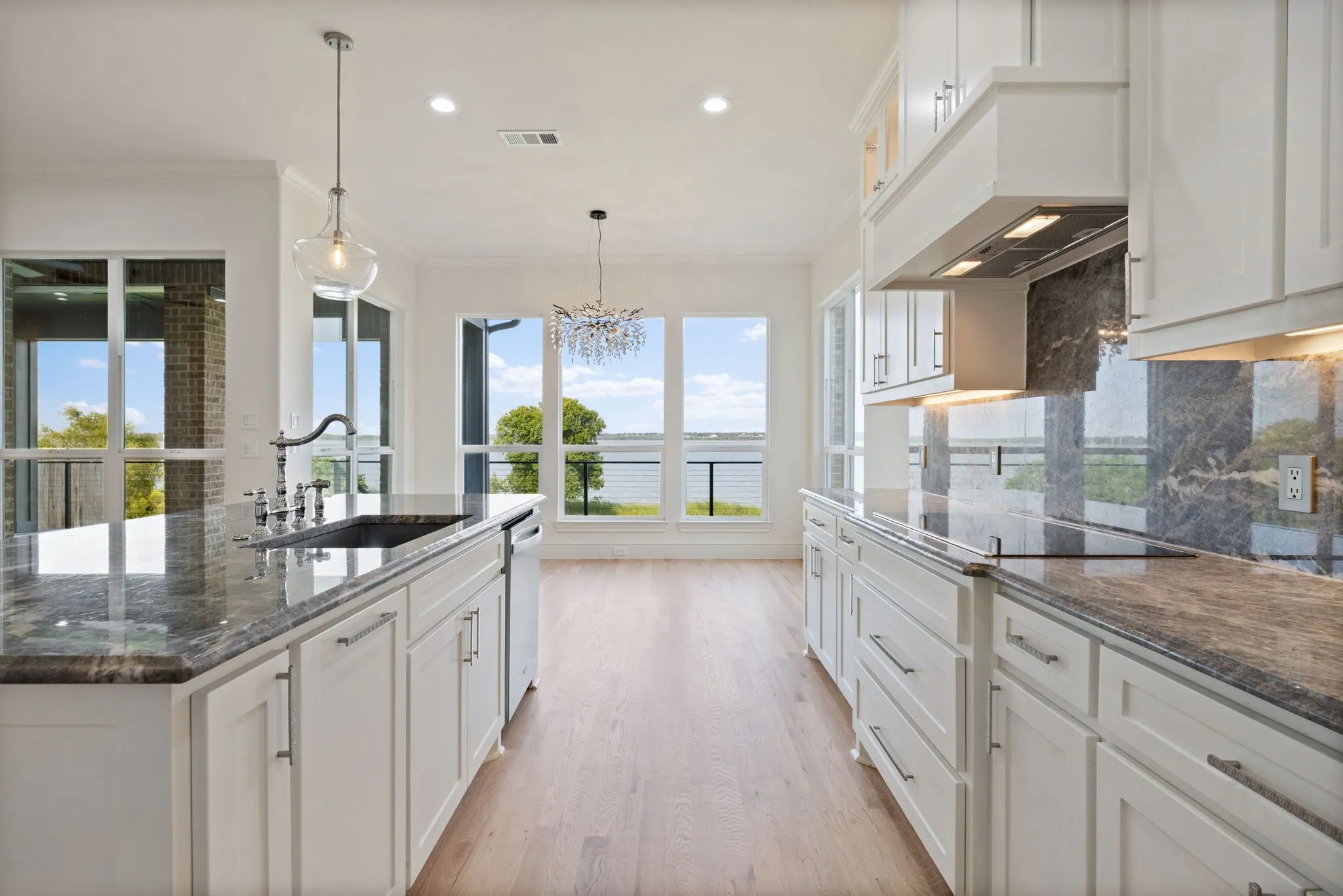 Modern kitchen featuring white cabinetry, stone countertops, a large center island with an undermount sink, and wood-finish flooring