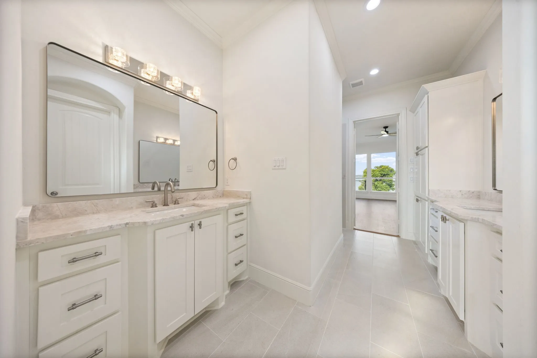Dual vanity bathroom featuring light-toned countertops, white cabinetry with chrome hardware, and a large wall-mounted mirror