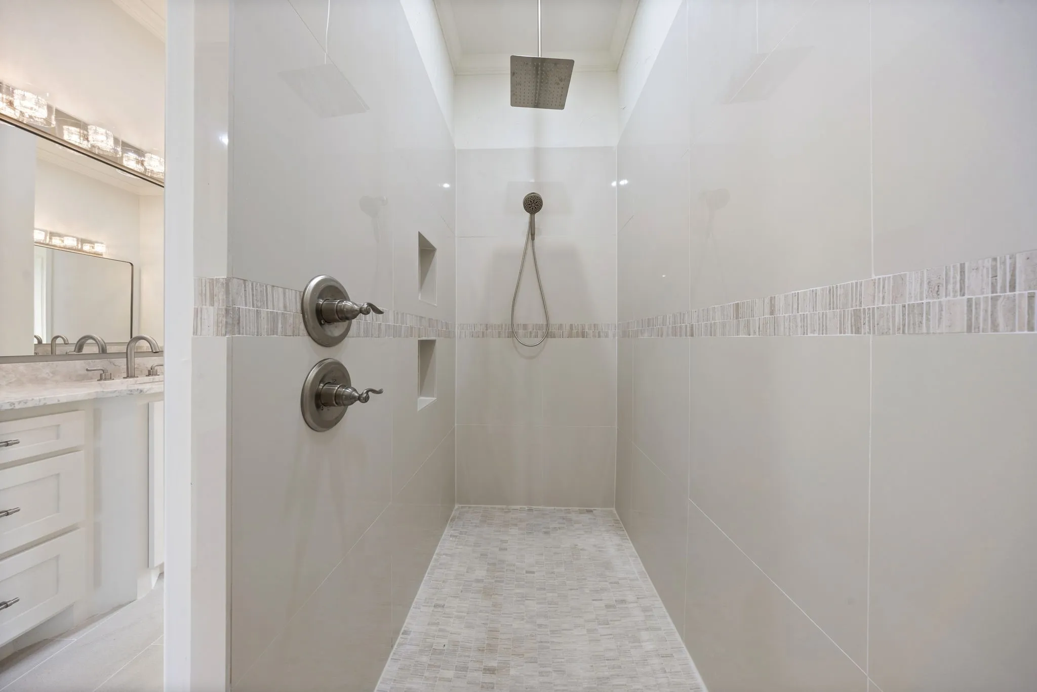 Walk-in shower featuring a square rainfall showerhead, handheld shower fixture, and dual recessed shelving