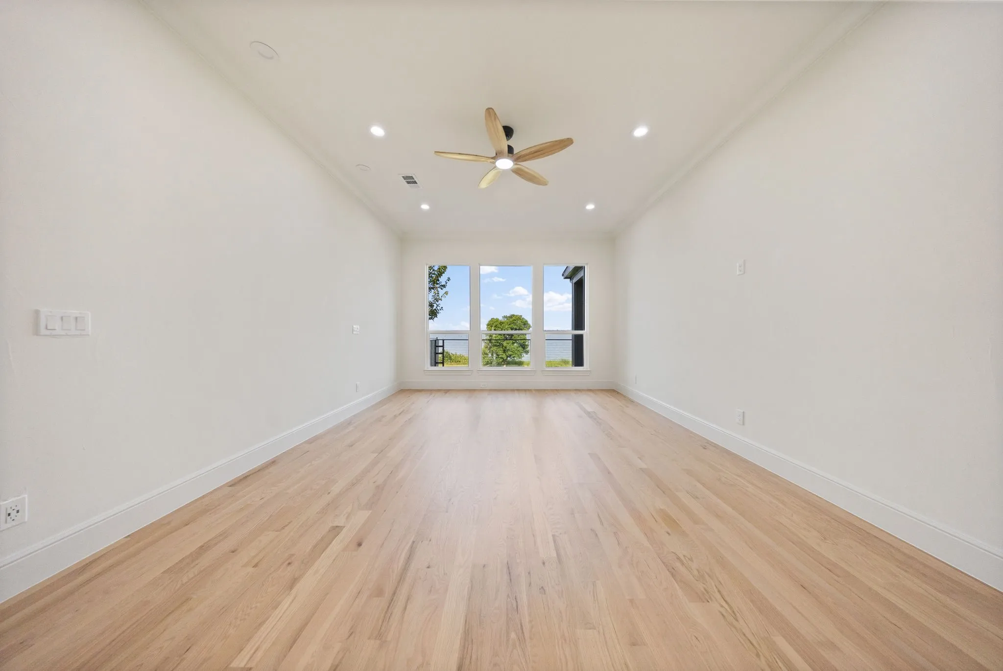 Spacious room featuring light wood-finish flooring, recessed lighting, and a modern ceiling fan