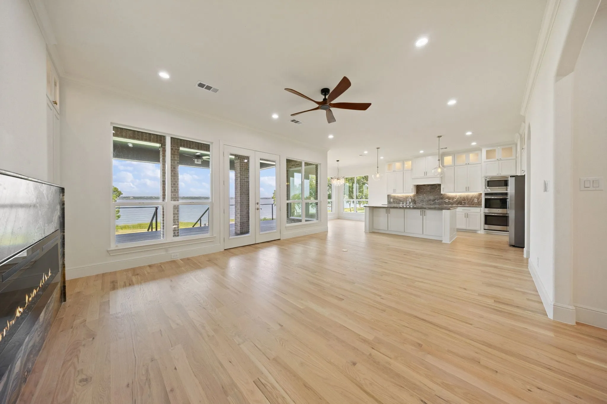 Spacious living area featuring light wood-finish flooring, a contemporary fireplace, and abundant natural light from large windows and glass doors