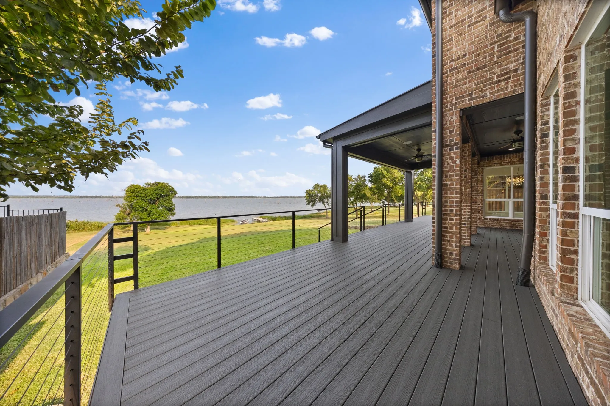 Expansive outdoor deck featuring dark composite decking, black metal cable railing, and a covered patio area with ceiling fans