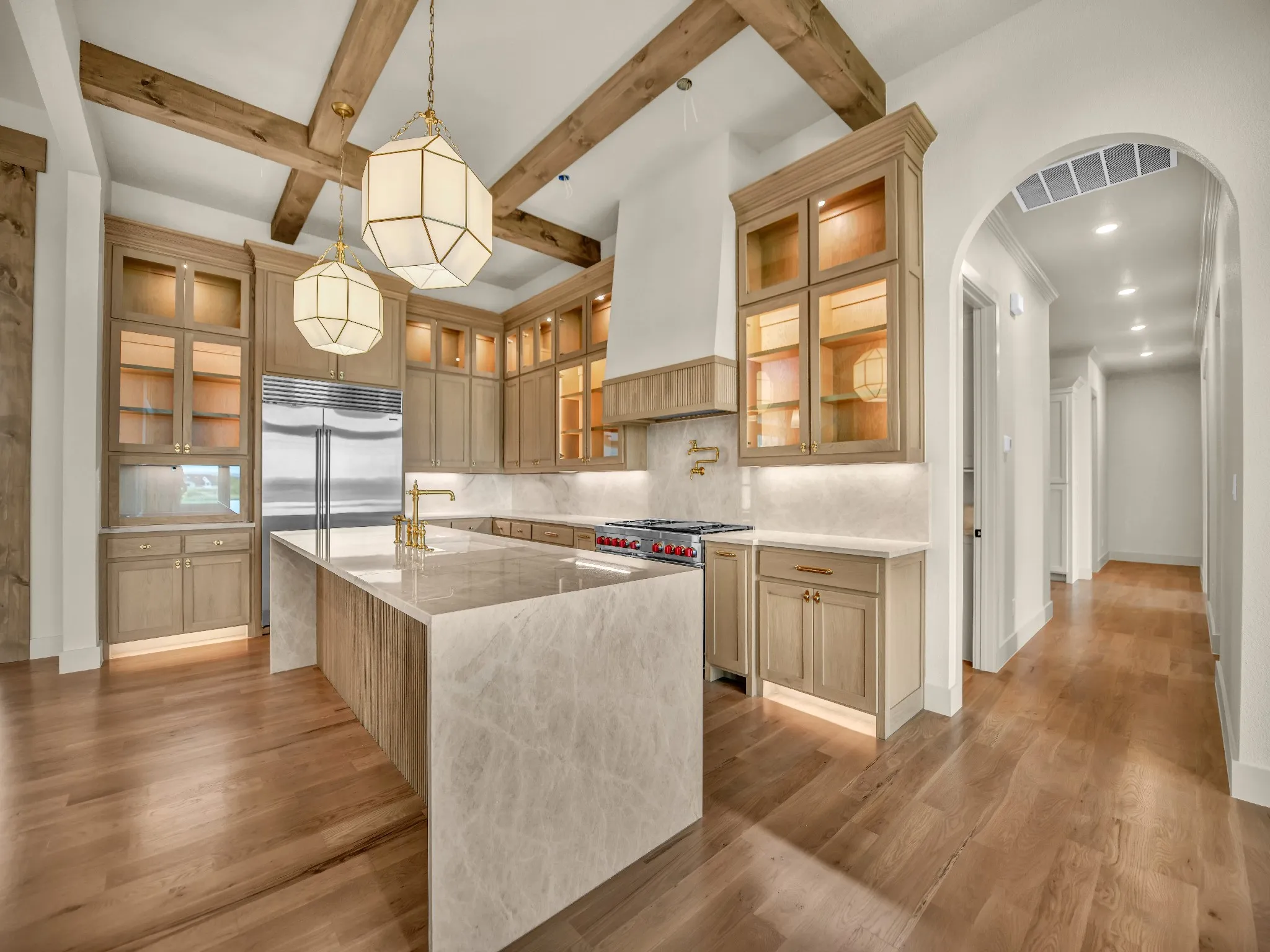 Kitchen featuring wood-finish flooring, exposed ceiling beams, a waterfall island, stainless steel appliances, and custom cabinetry with glass-front uppers