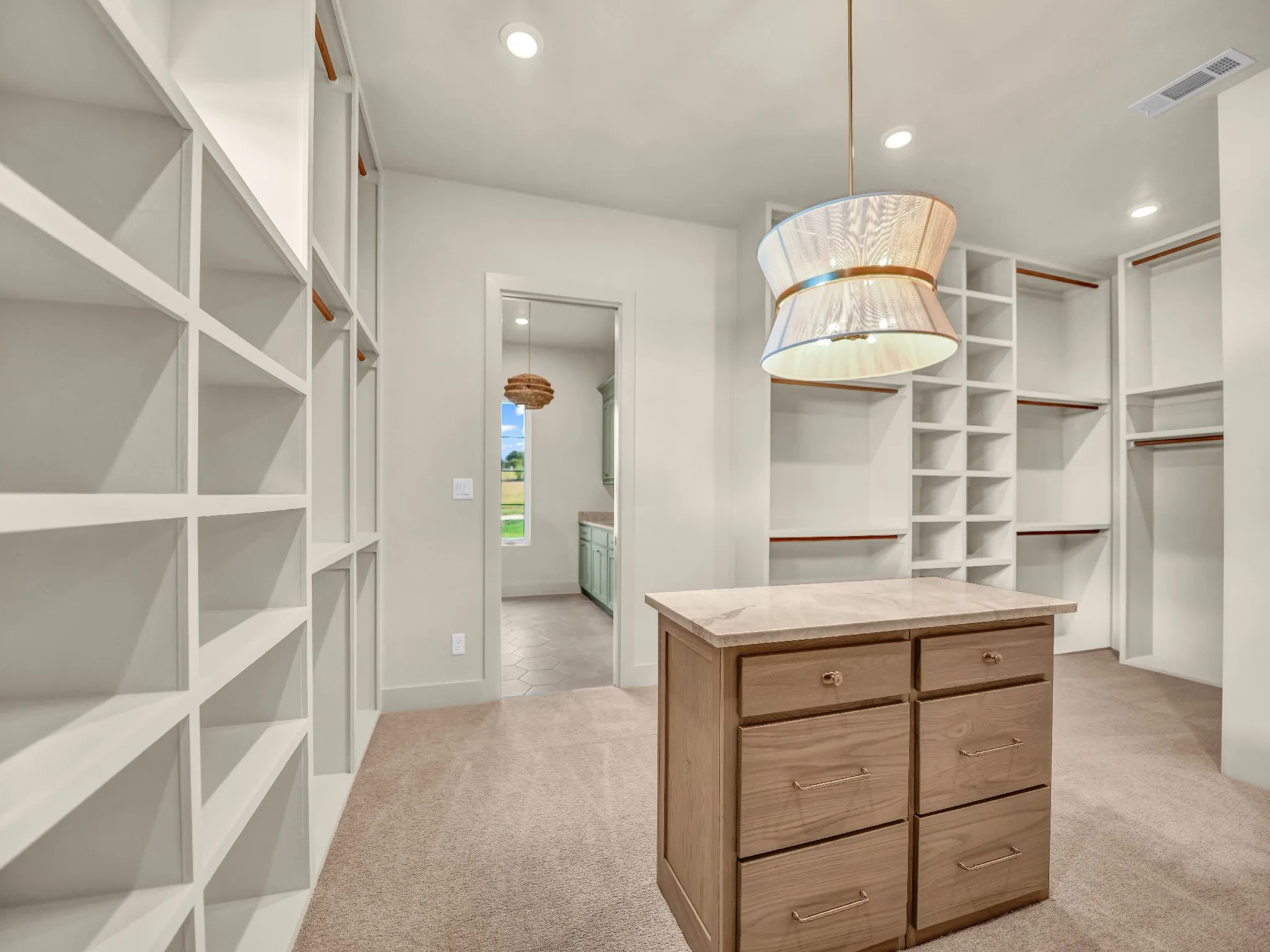Built-in shelving, hanging rods, central wood-finish island with drawers, recessed lighting, and a decorative pendant light