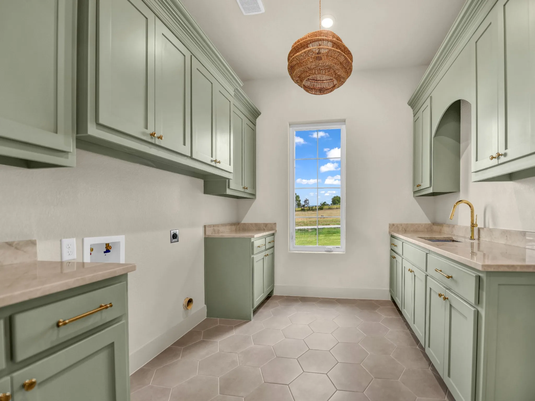 Hexagonal floor tiling, extensive cabinetry with brass hardware, light-colored countertops, single-pane window, and a built-in sink with a gold-finish faucet