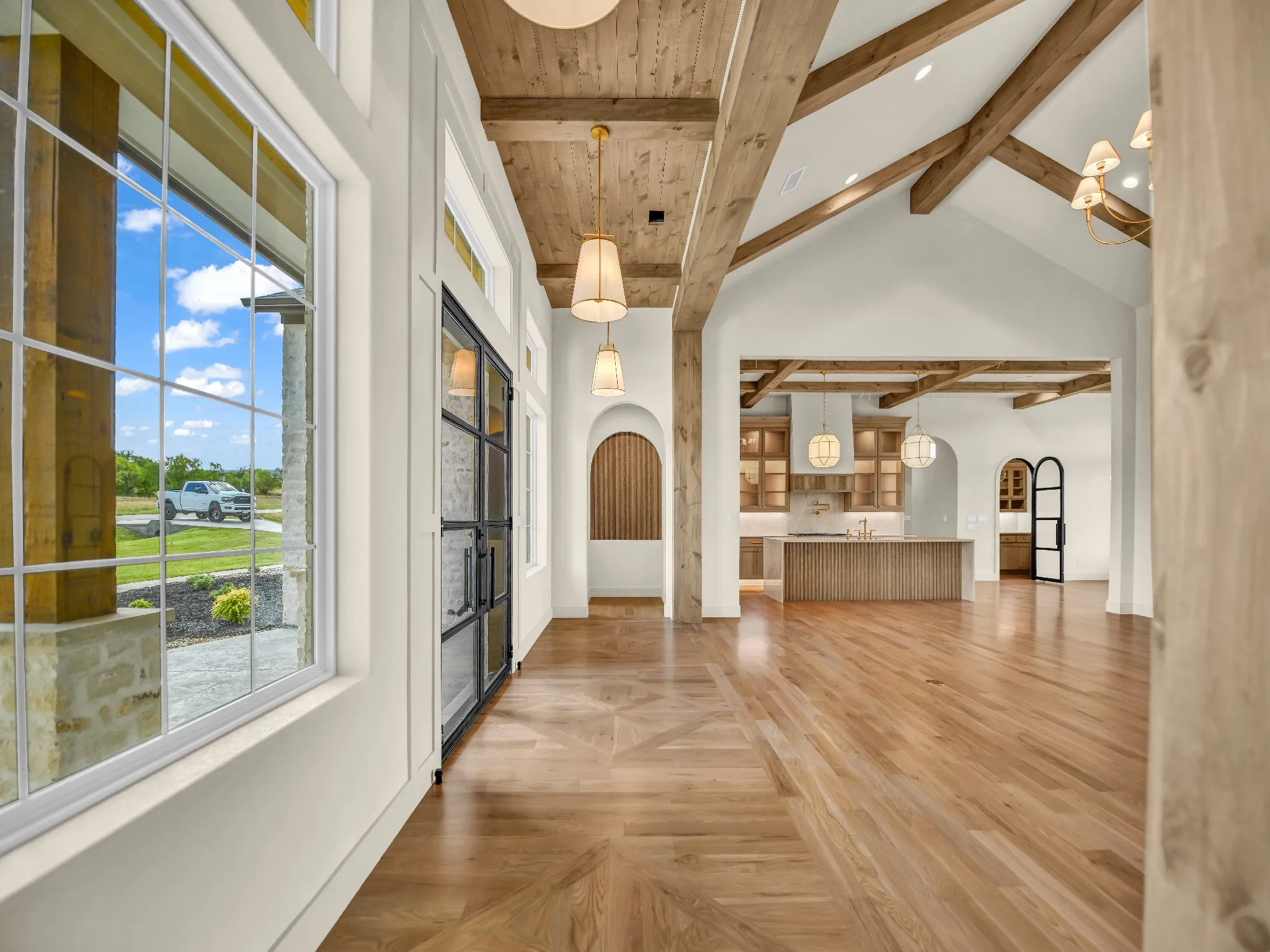 Hardwood flooring with a patterned inlay, exposed wood beam ceiling, vaulted ceilings, pendant lighting, and an arched doorway