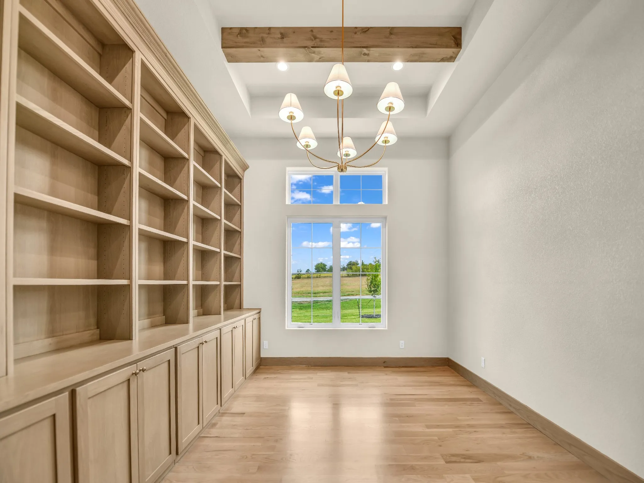 Built-in shelving with lower cabinetry, wood-finish flooring, a decorative ceiling beam, and a multi-light chandelier