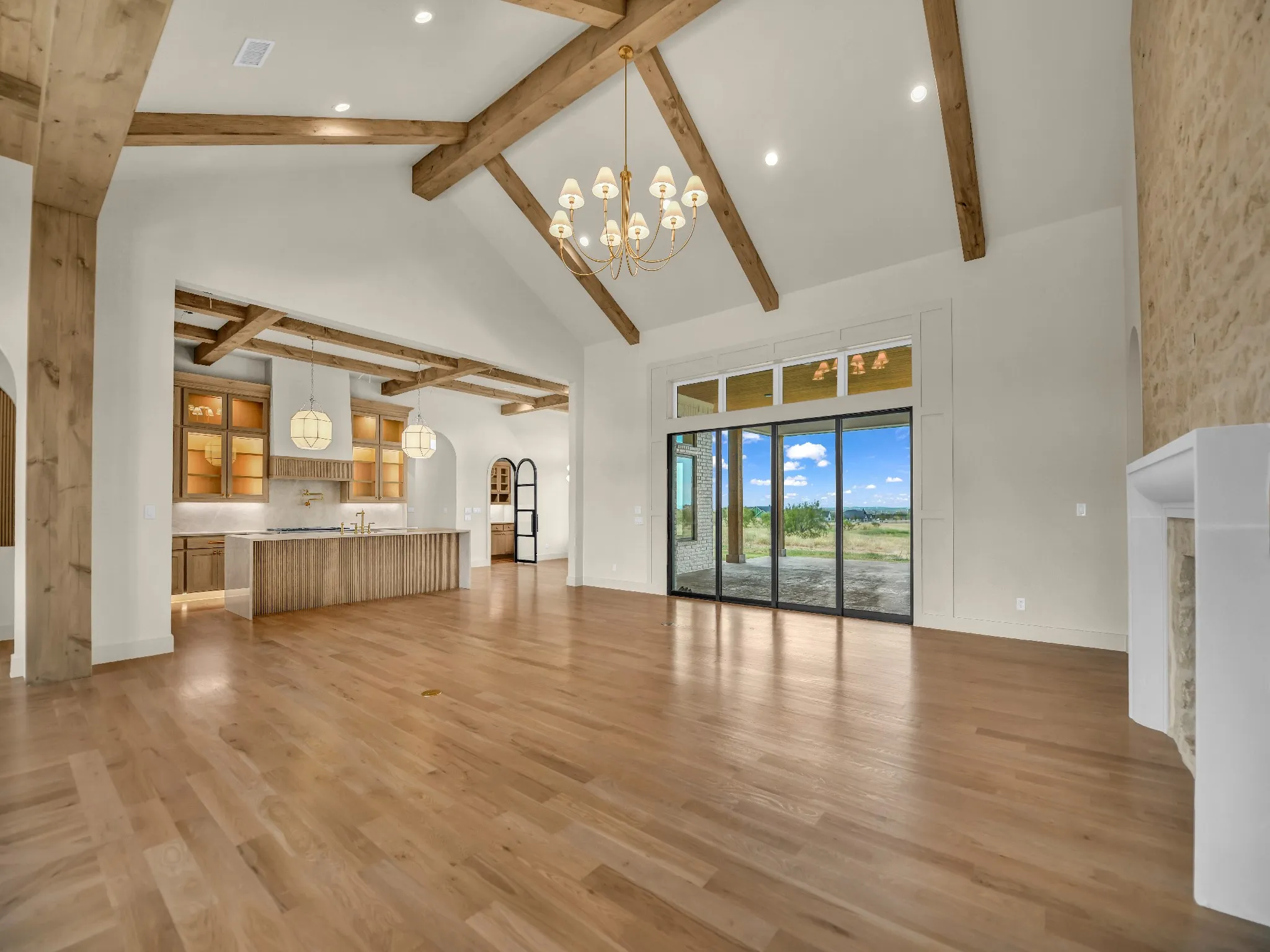 Vaulted ceilings with exposed wood beams, hardwood flooring, fireplace with stone surround, custom kitchen cabinetry, and large sliding glass doors