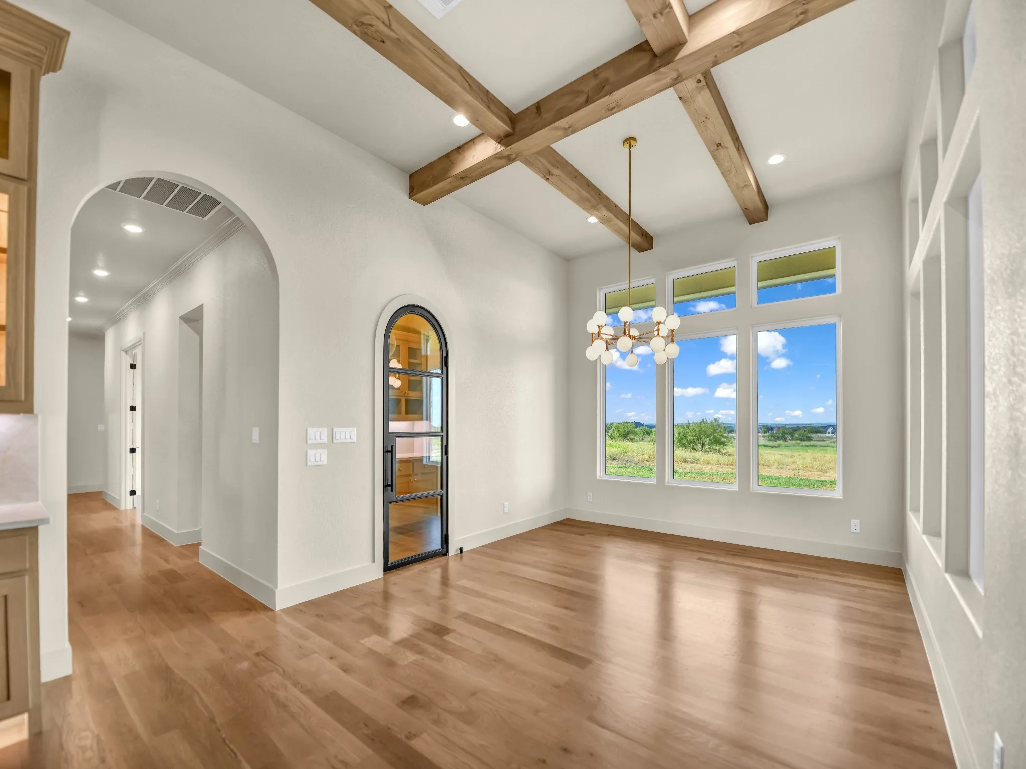 Vaulted ceiling with wood beams, wood-finish flooring, floor-to-ceiling windows, arched entryways, and a contemporary chandelier