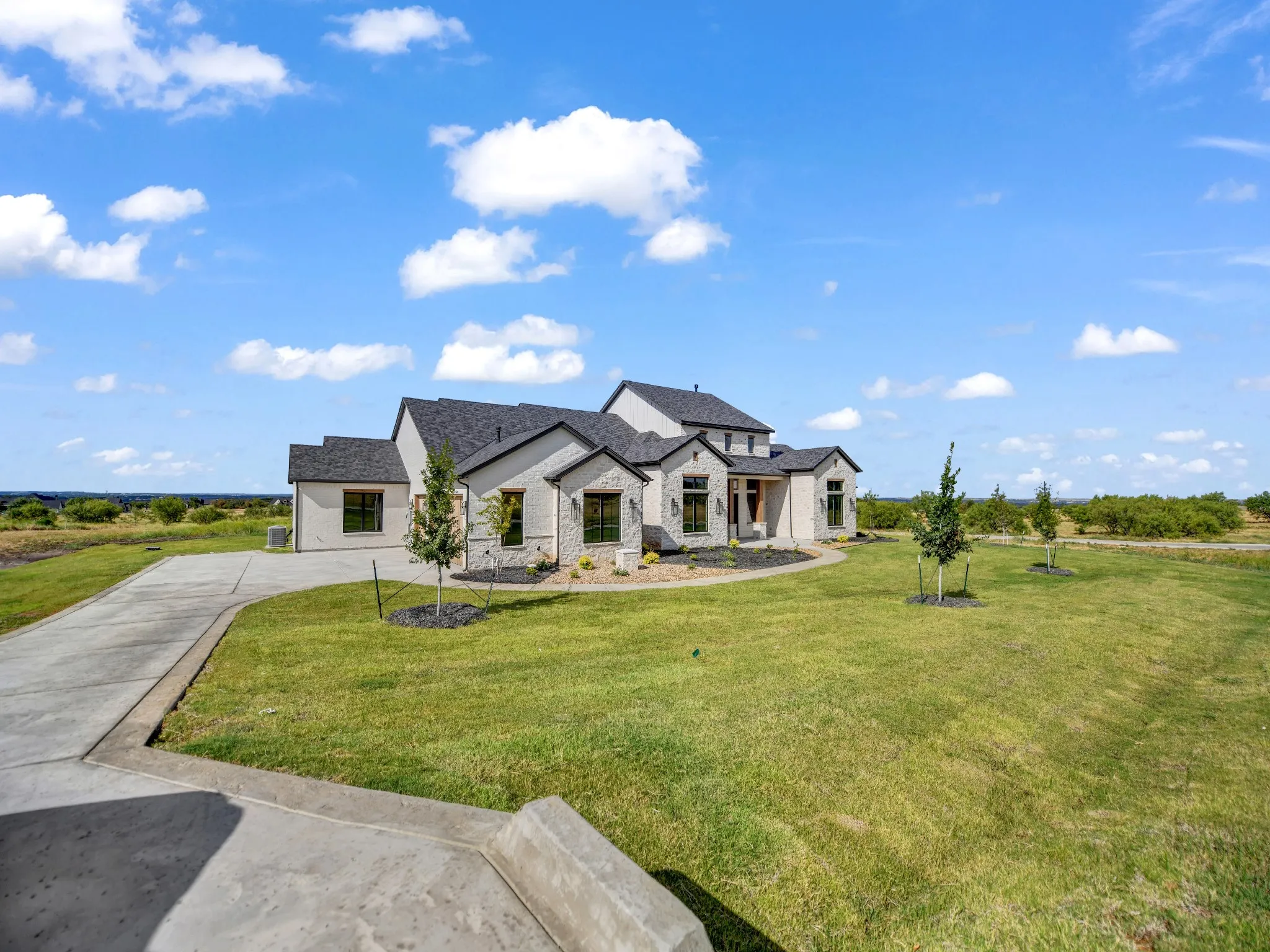 Stone exterior with dark-framed windows, a dark shingle roof, and an expansive lawn