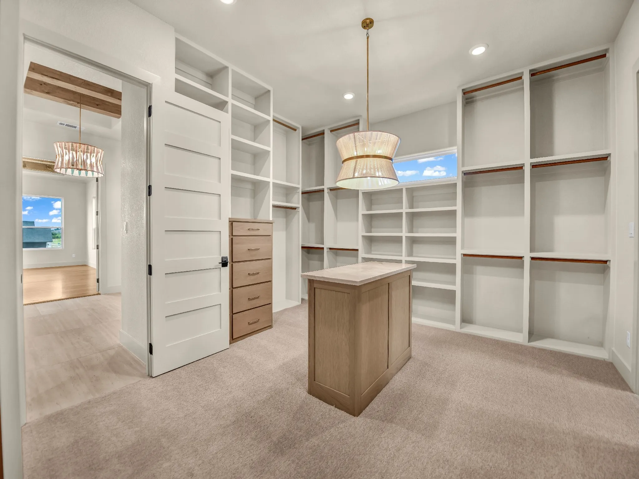 Spacious walk-in closet featuring extensive built-in shelving, a central wood-finish island, built-in dresser with five drawers, and a decorative pendant light fixture