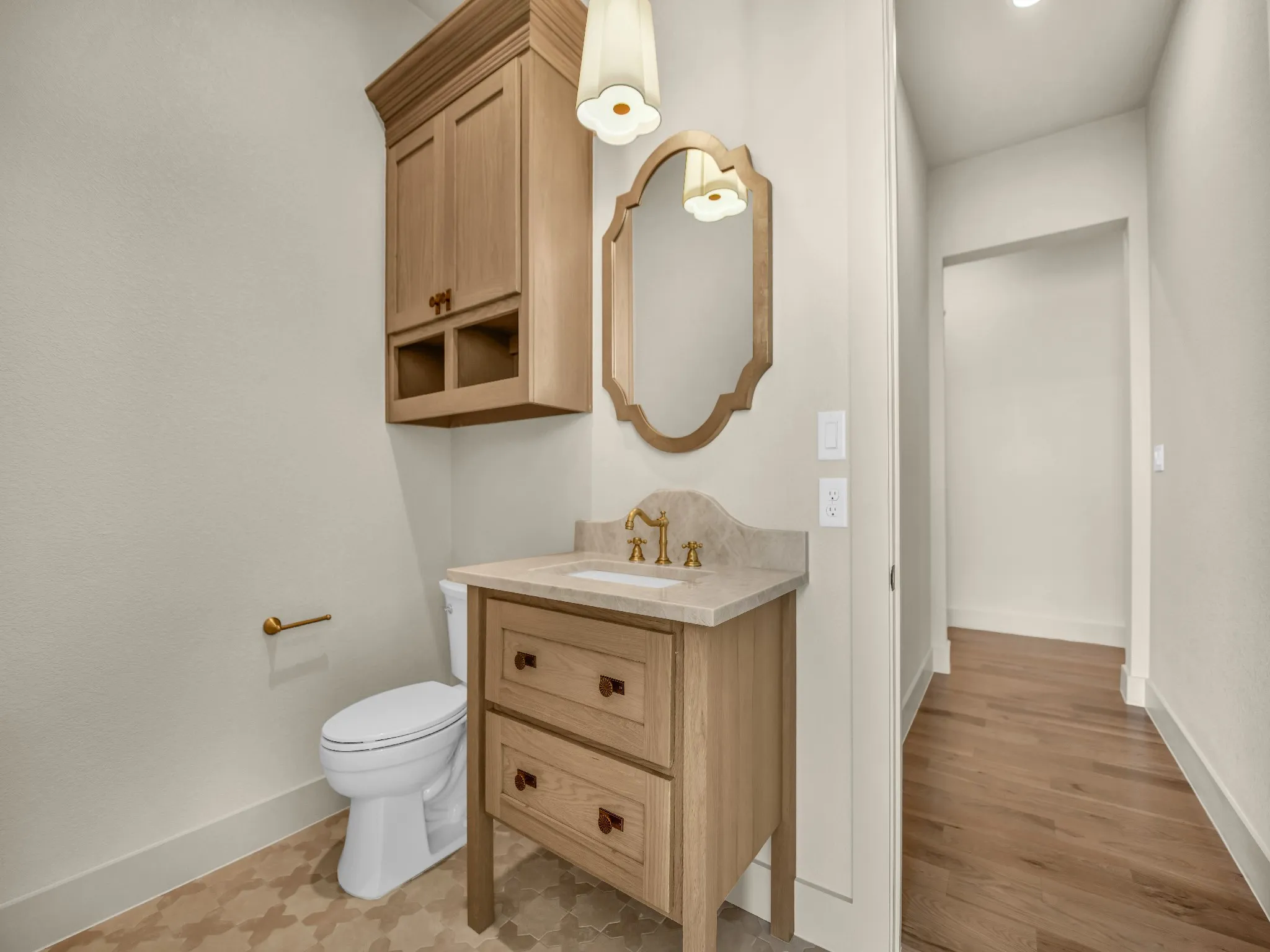 Light wood-finish vanity with stone countertop, brass-finish faucet, and patterned floor tile