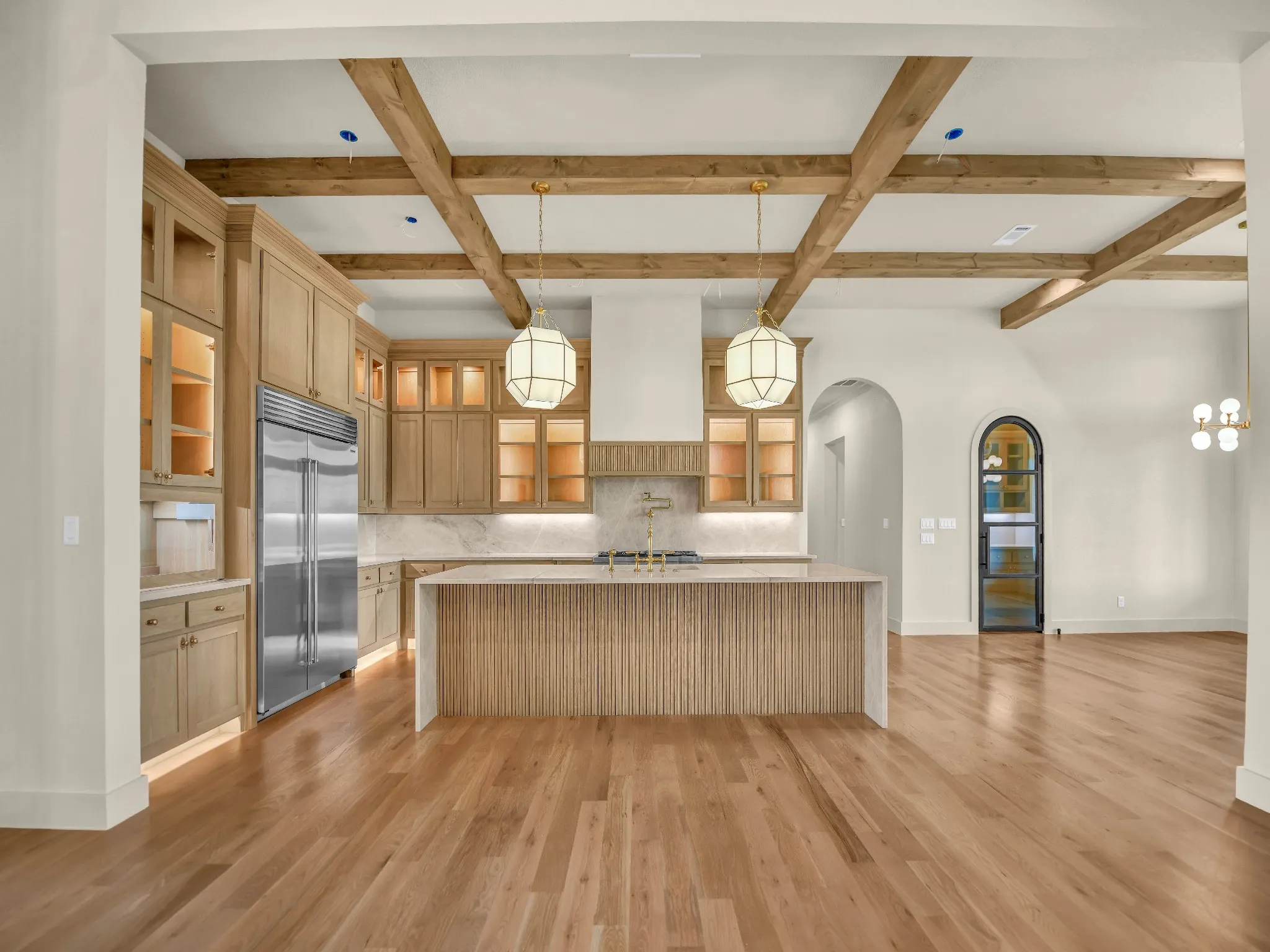 Hardwood flooring, custom wood cabinetry, exposed ceiling beams, large kitchen island with fluted detailing, and arched doorways