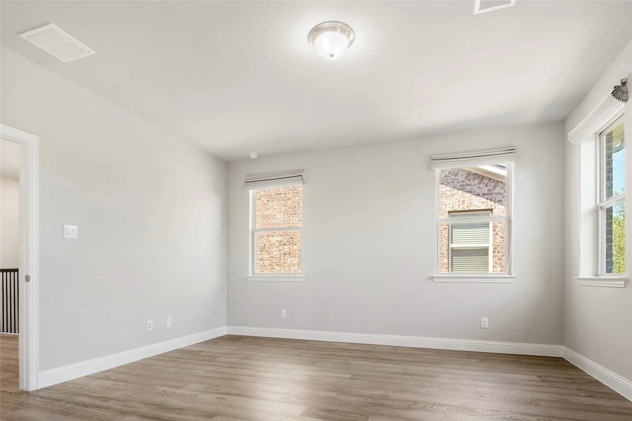 Spacious room featuring wood-finish flooring, light gray wall paint, and white baseboards