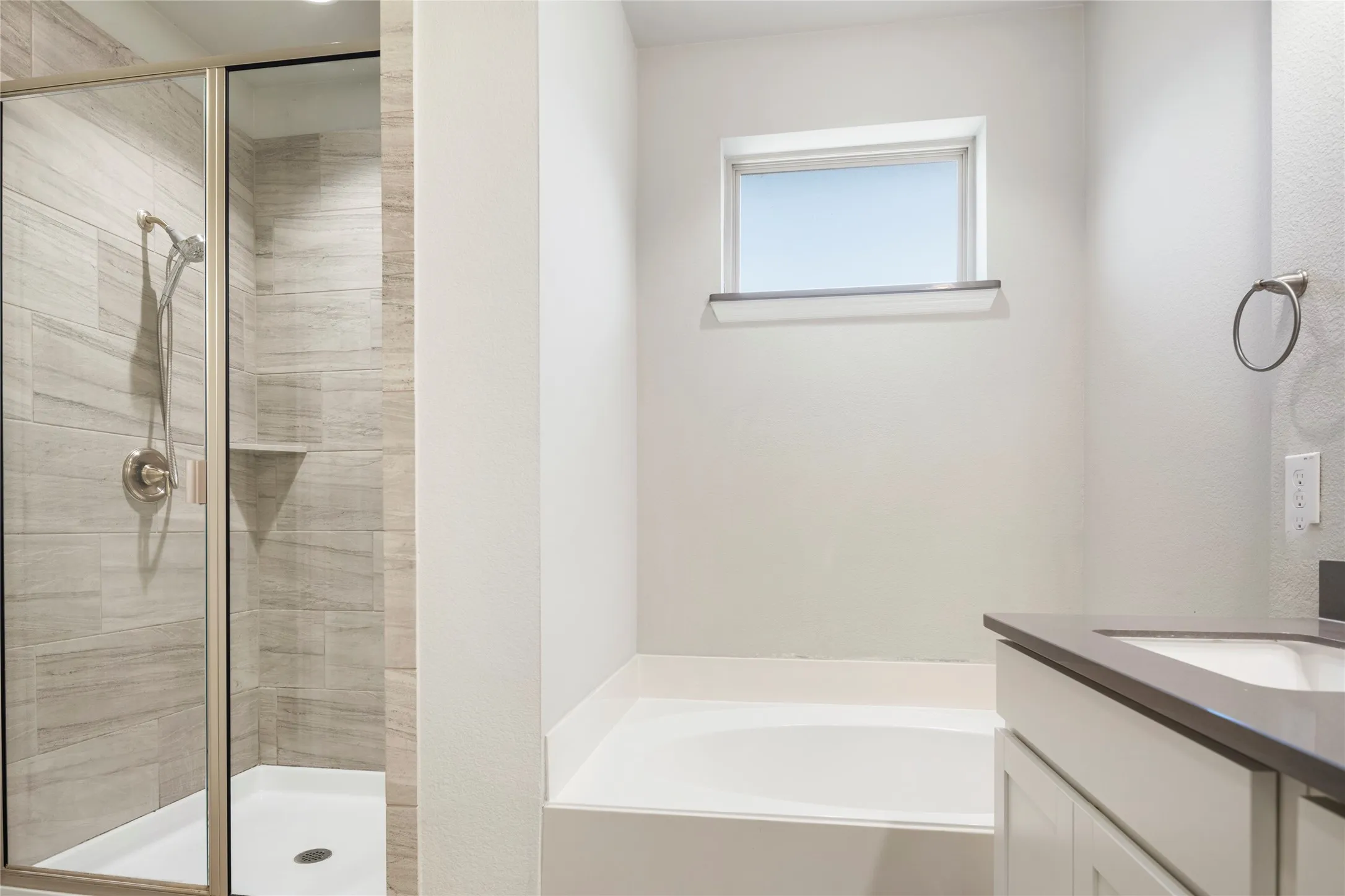 Contemporary bathroom featuring a glass-enclosed shower with tiled walls and a built-in shelf, a deep soaking tub, a vanity with a dark countertop and undermount sink, and a high-set window