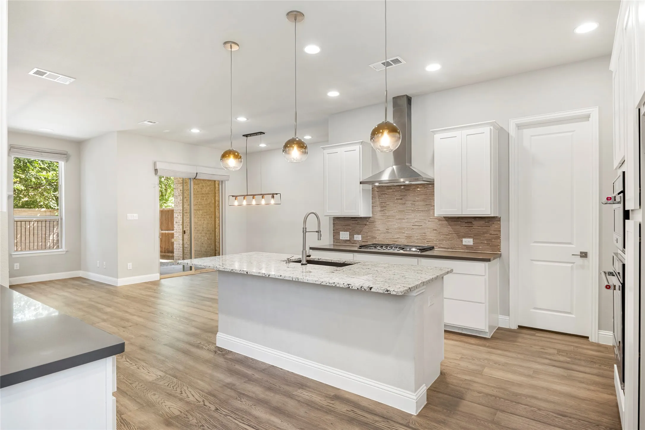 Modern kitchen featuring a large center island with a stone countertop and integrated sink, white shaker cabinetry, stainless steel appliances, and a tiled backsplash