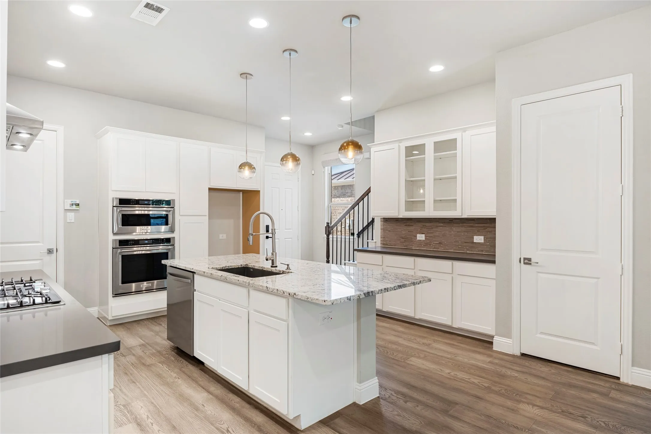 Spacious kitchen featuring an island with a sink, stainless steel dishwasher, and light-toned stone countertop