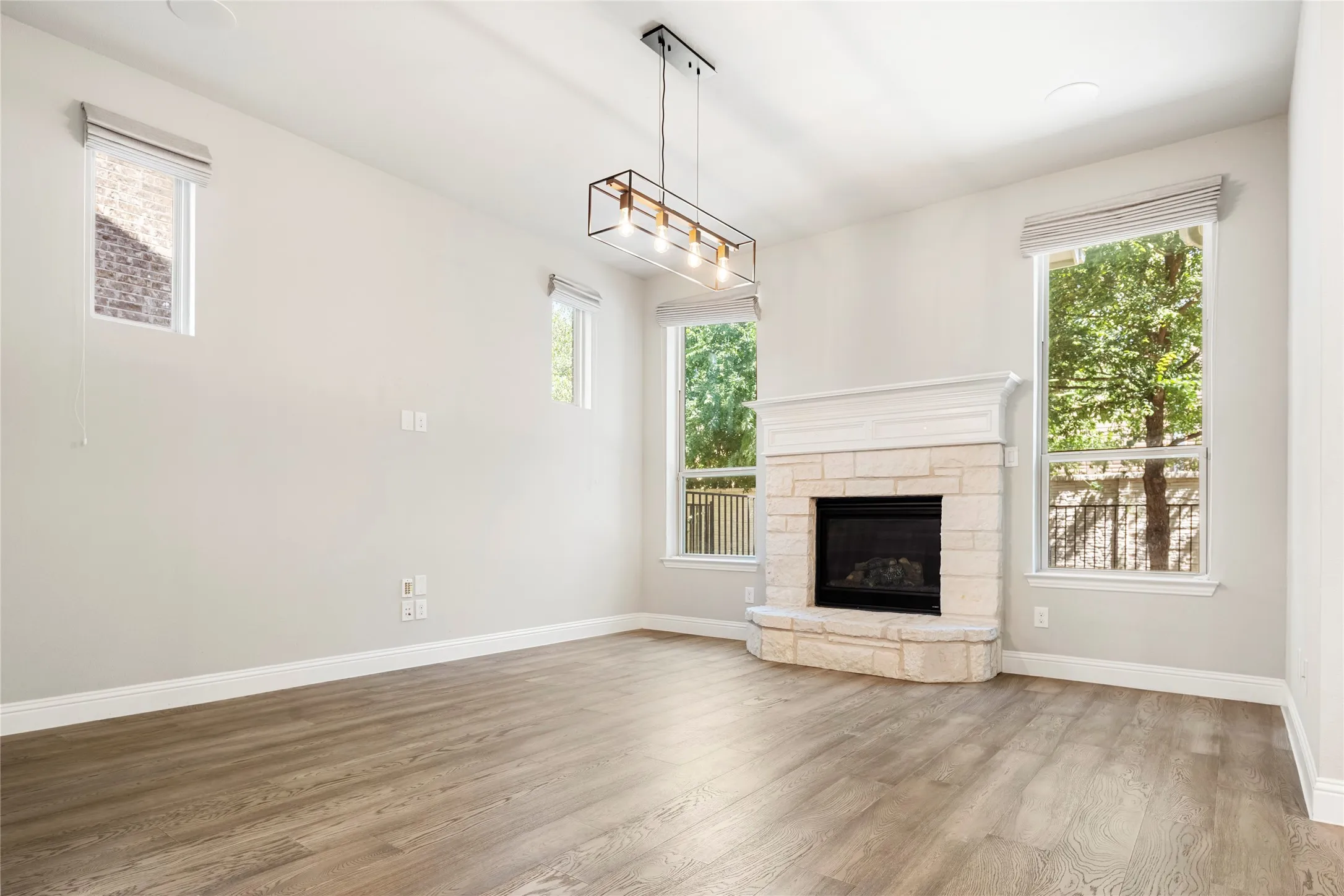 Living space featuring a corner stone fireplace with a white mantel, wood-finish flooring, and multiple windows