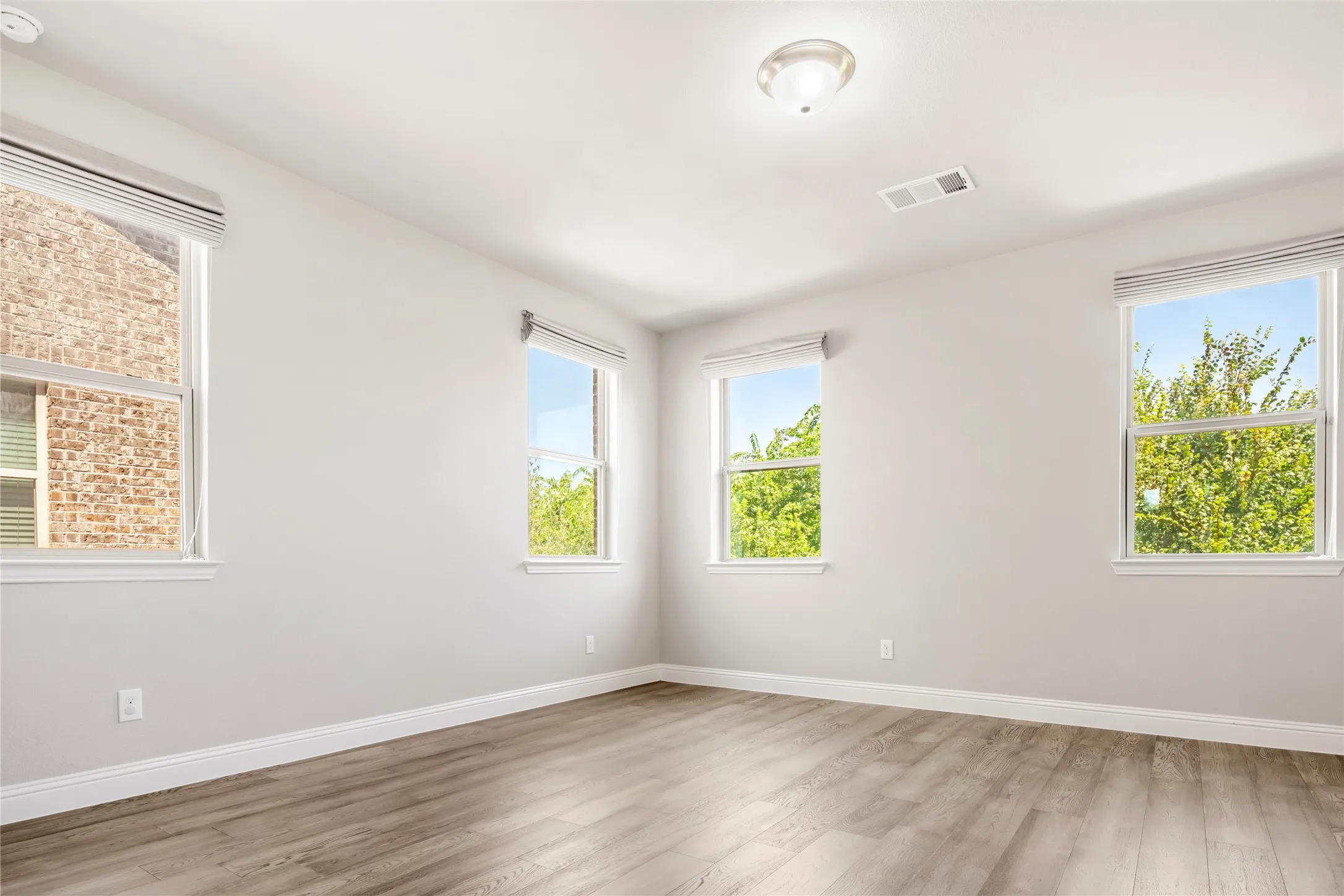 Bright room featuring four windows with blinds, light gray wall paint, white trim, and wood-finish flooring