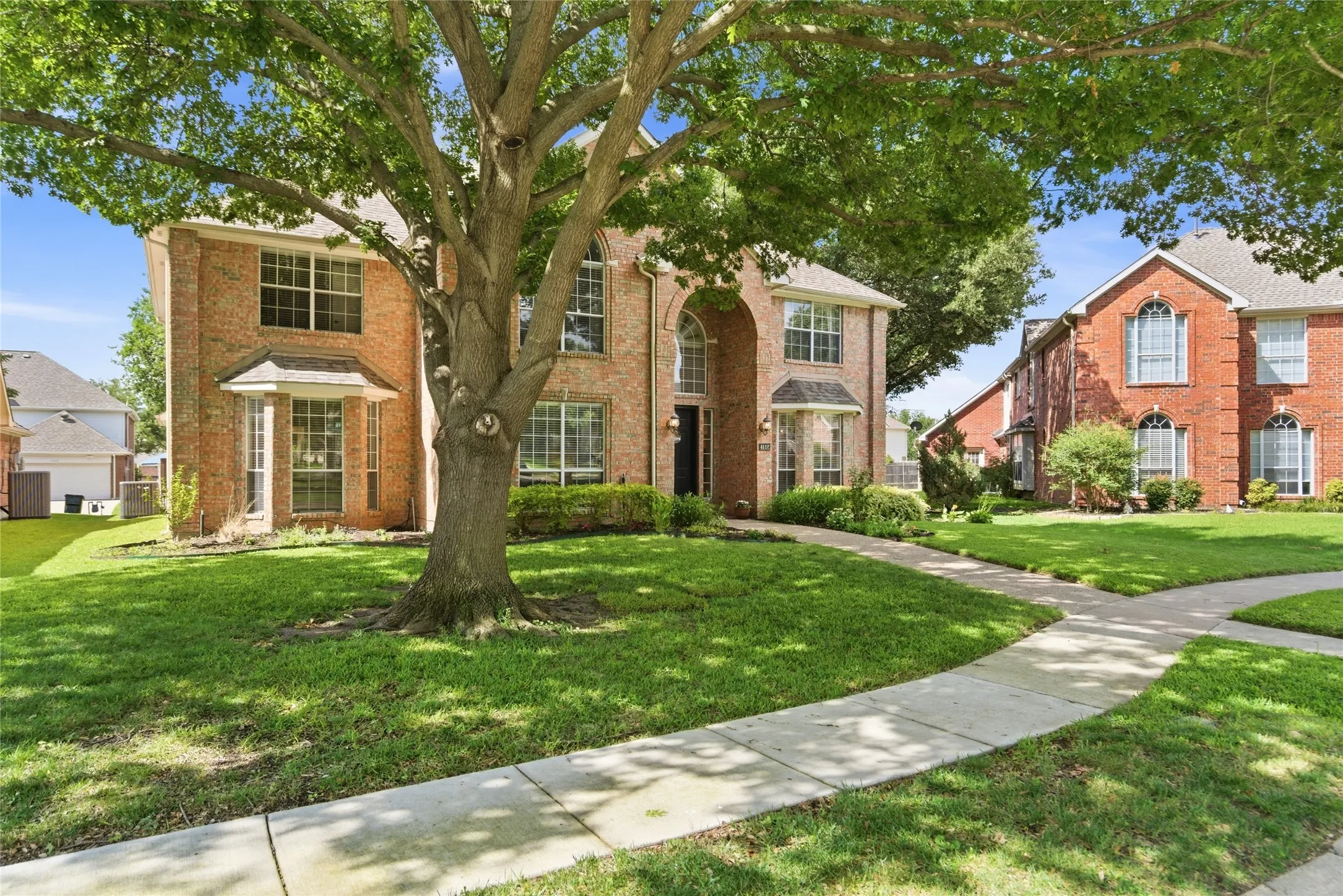 Brick exterior with multiple bay windows, an arched entry, and a mature tree providing shade