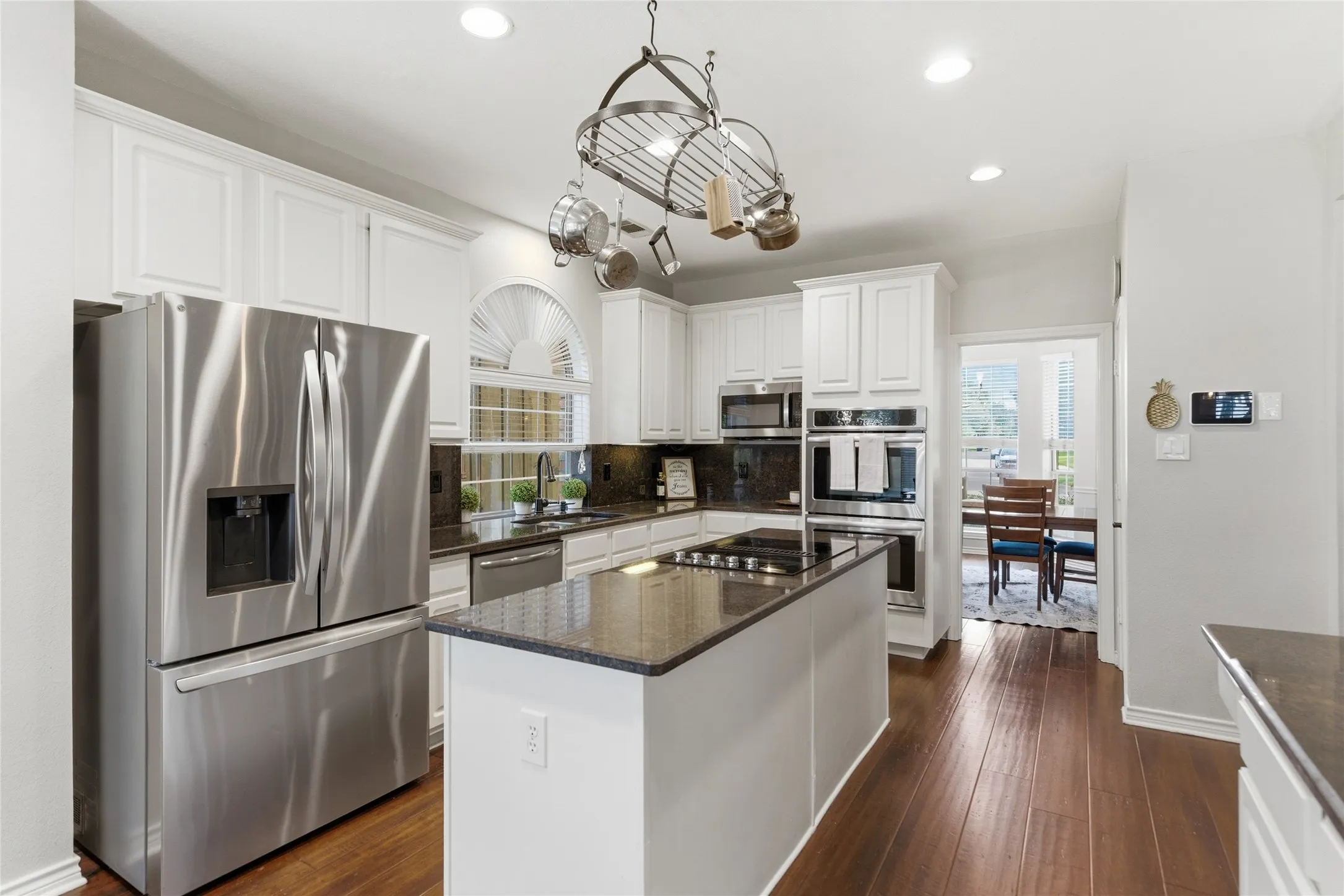 Gourmet kitchen featuring white cabinetry, stainless steel appliances, dark stone countertops, wood-finish flooring, and a central island with a cooktop