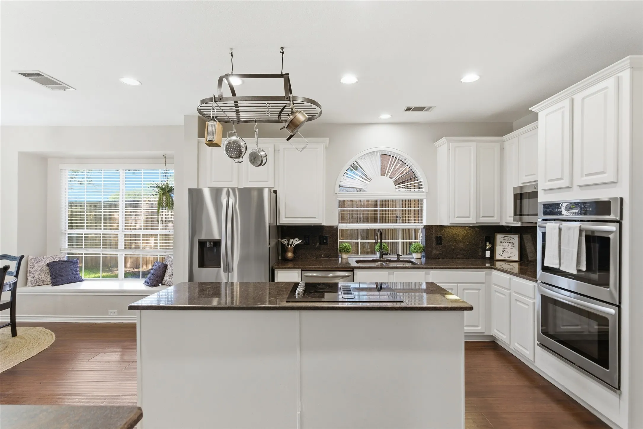 White cabinetry kitchen featuring a central island, stainless steel appliances, dark countertops, and wood-finish flooring