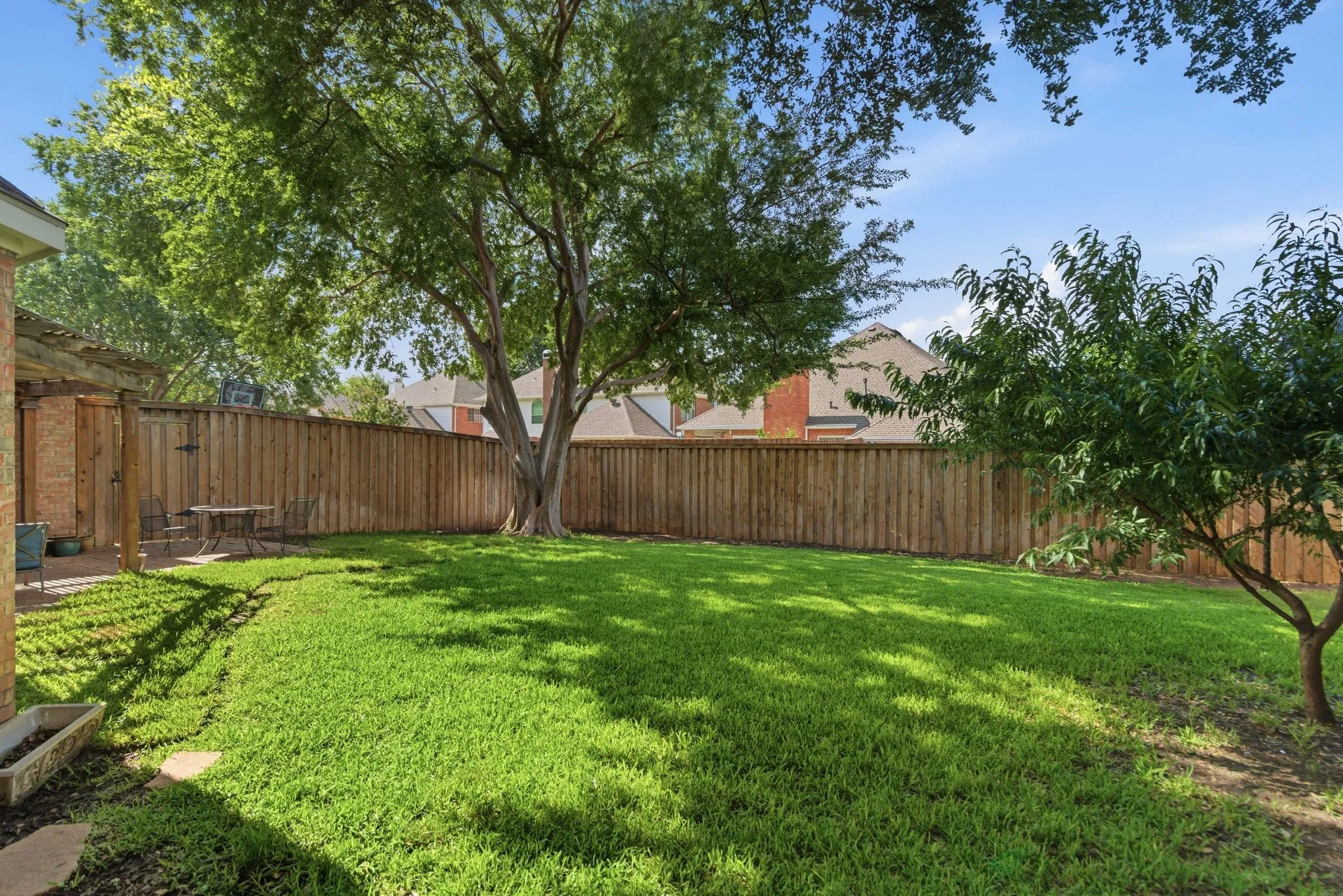 Expansive backyard featuring a large tree, lush green lawn, private wood fencing, and a brick patio with a pergola structure