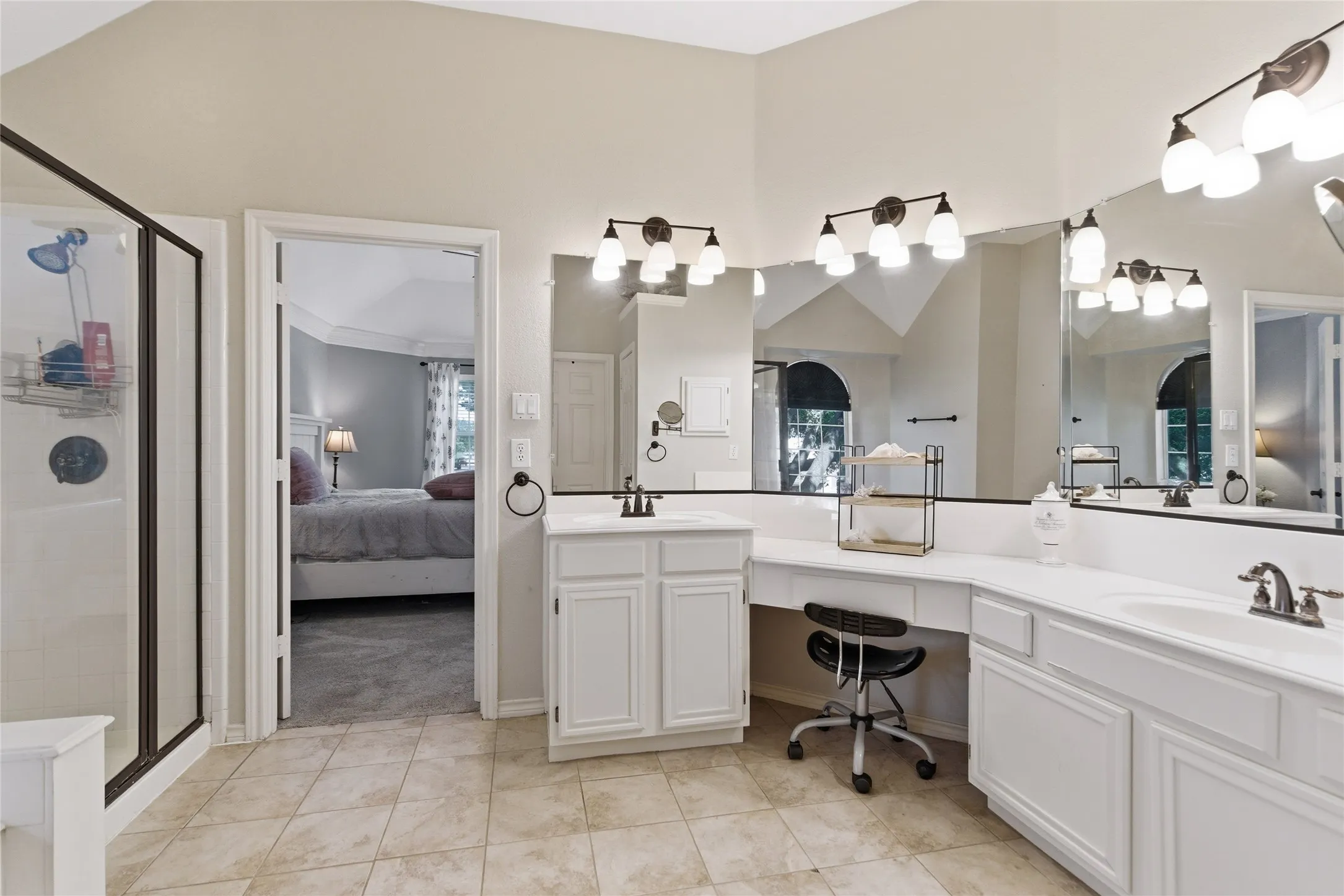 Bathroom featuring dual vanities, white cabinetry, extensive mirror coverage, a separate shower enclosure with a dark frame, and light-toned tile flooring