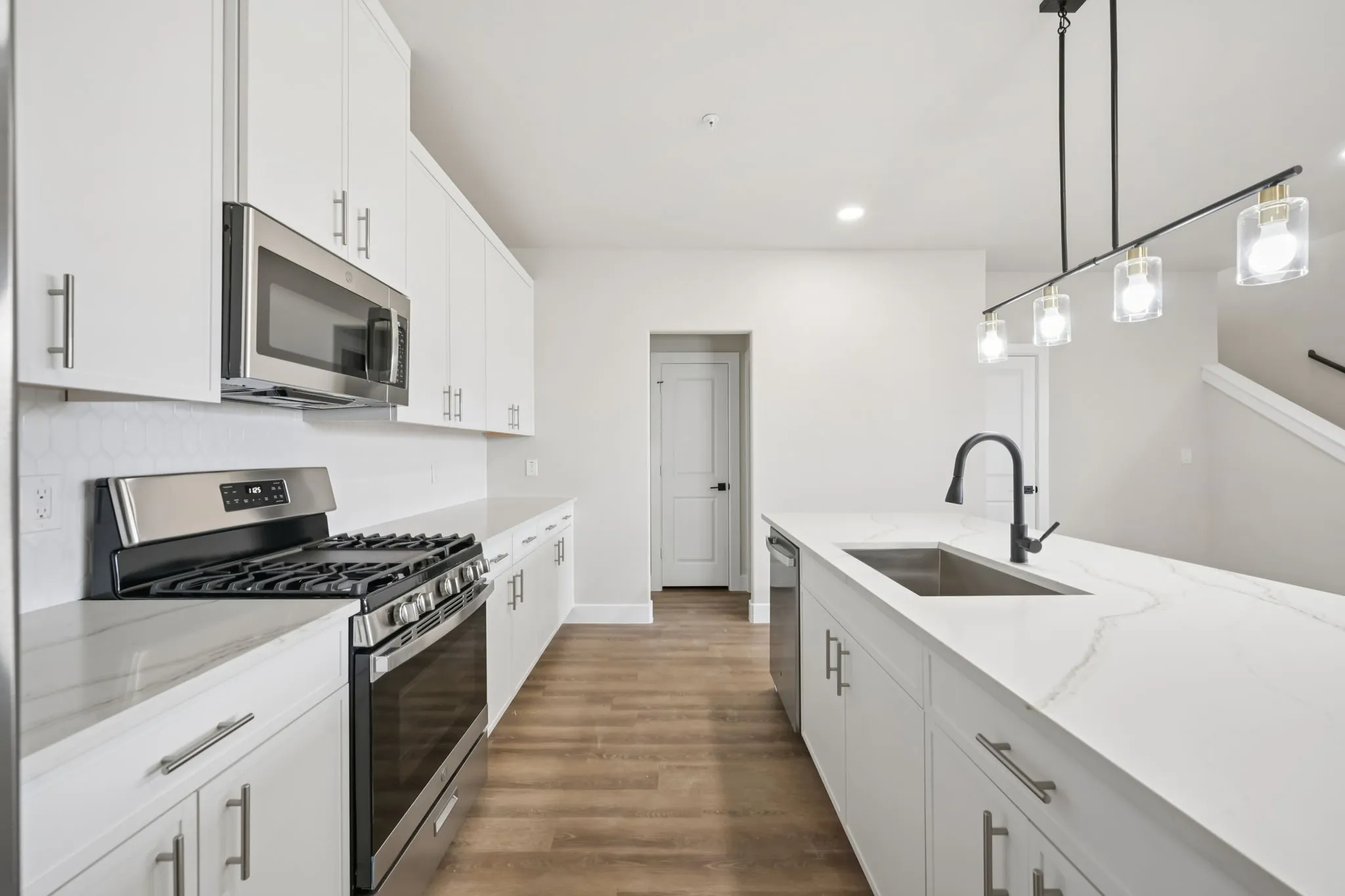 Modern kitchen featuring a large island with an undermount sink and matte black faucet, stainless steel appliances, white cabinetry, hexagon tile backsplash, and wood-finish flooring